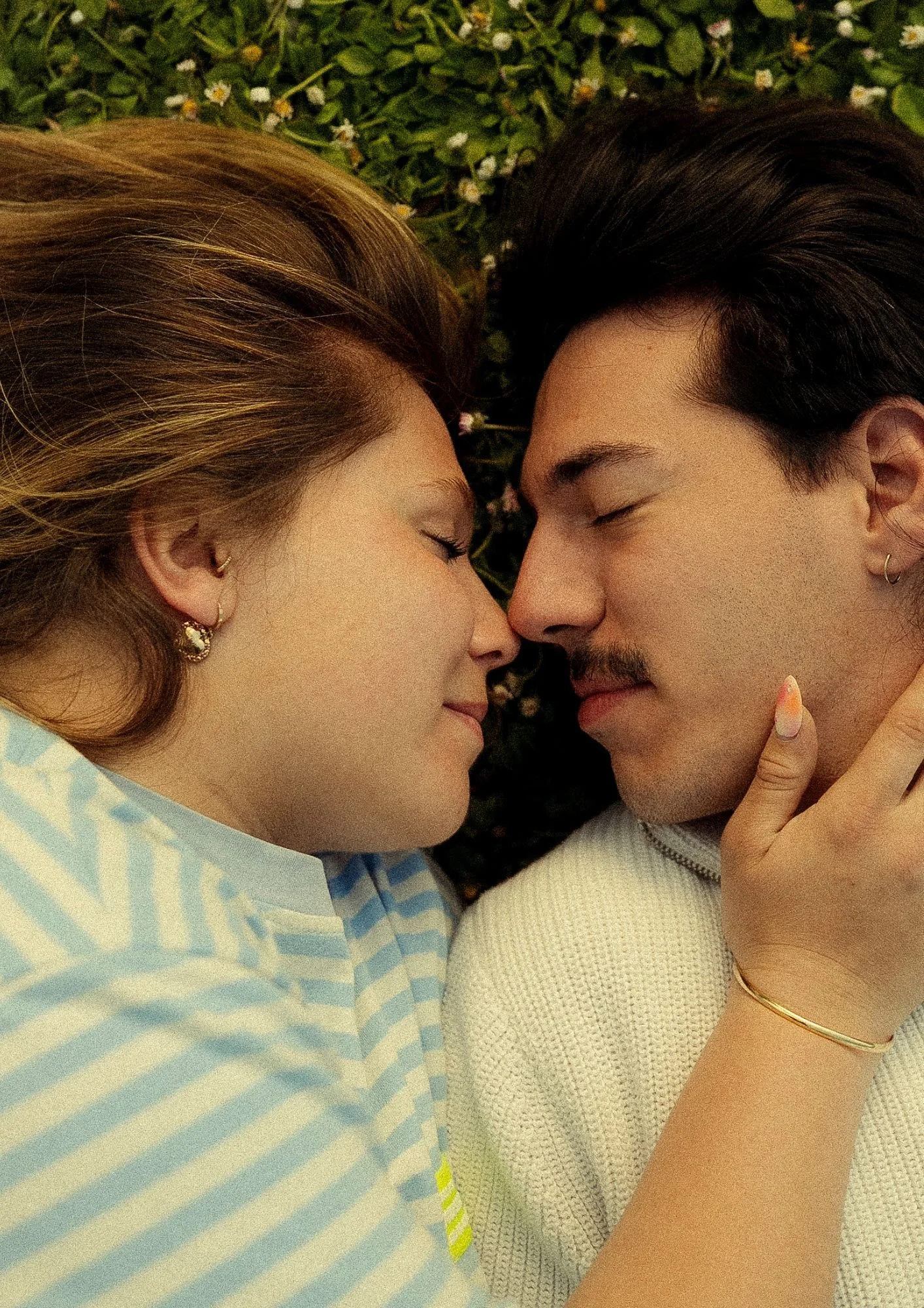 couple allongé dans l'herbe qui se font des caresses 