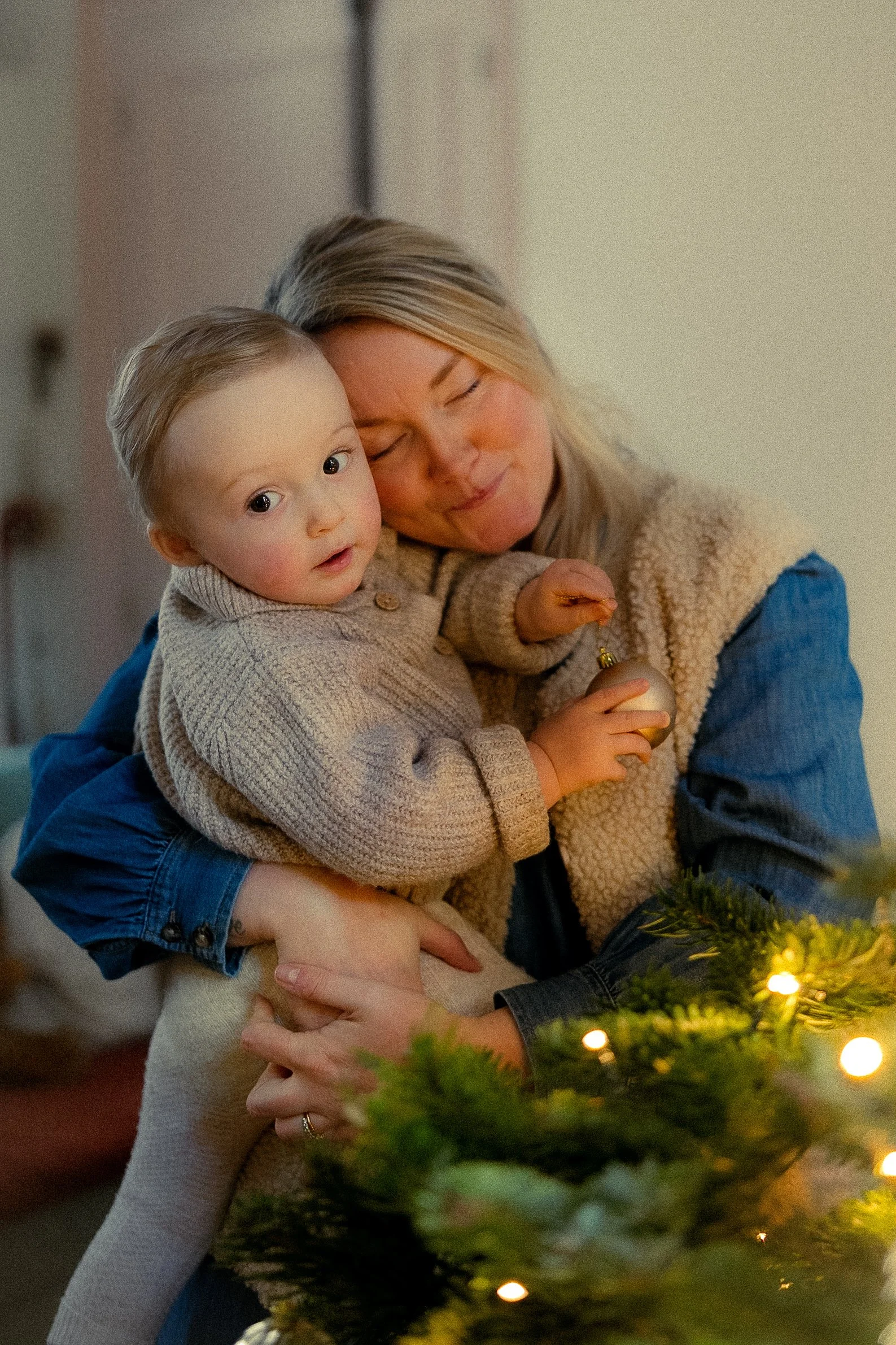 A woman and a young child sharing a hug during Christmas with a decorated tree and lights in the background.