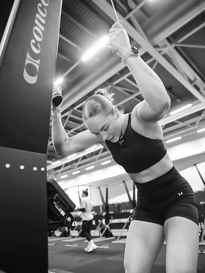 A woman in workout attire working out at a gym, lifting weights with a determined expression.