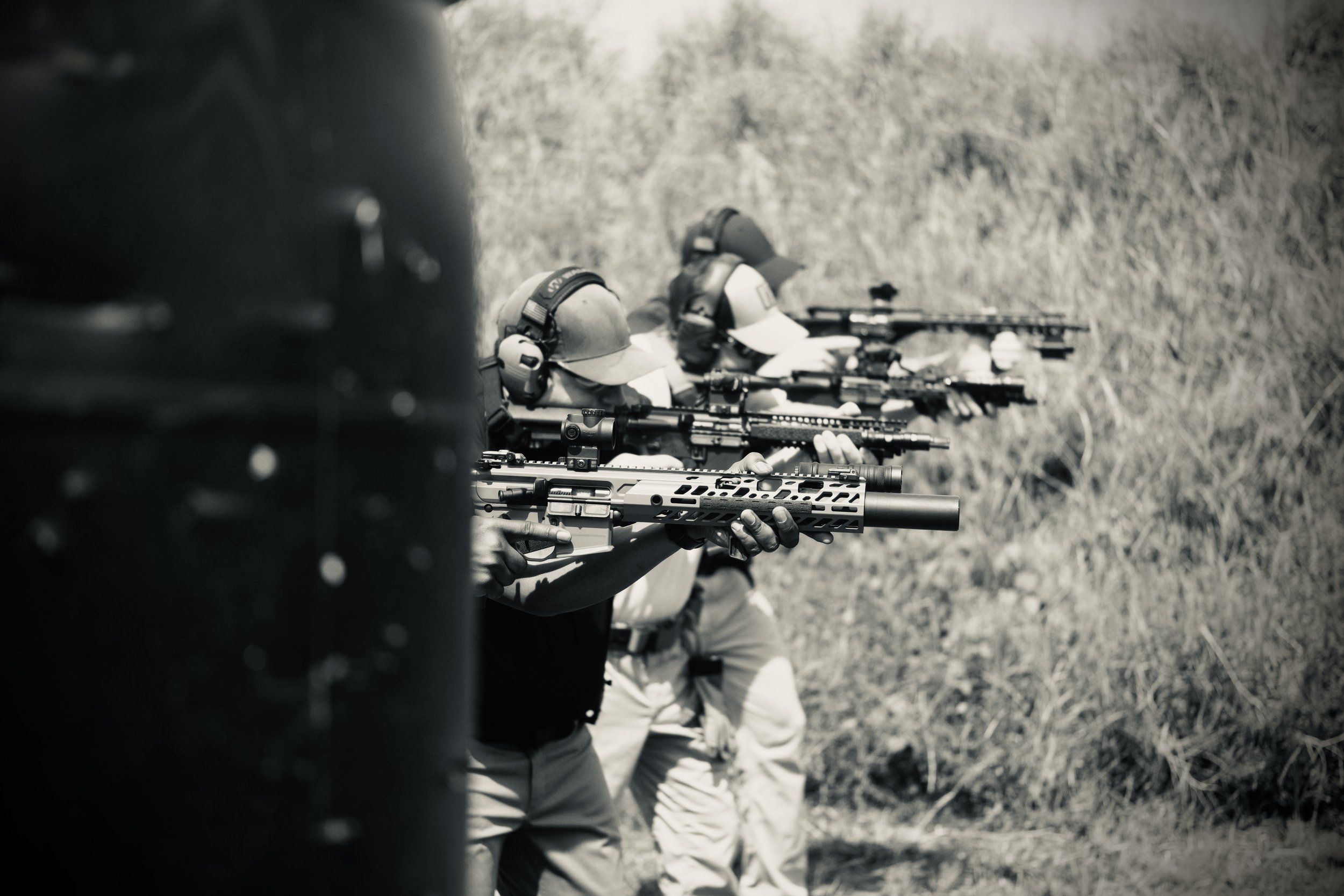 Two people in tactical gear aiming rifles during a shooting practice outdoors.