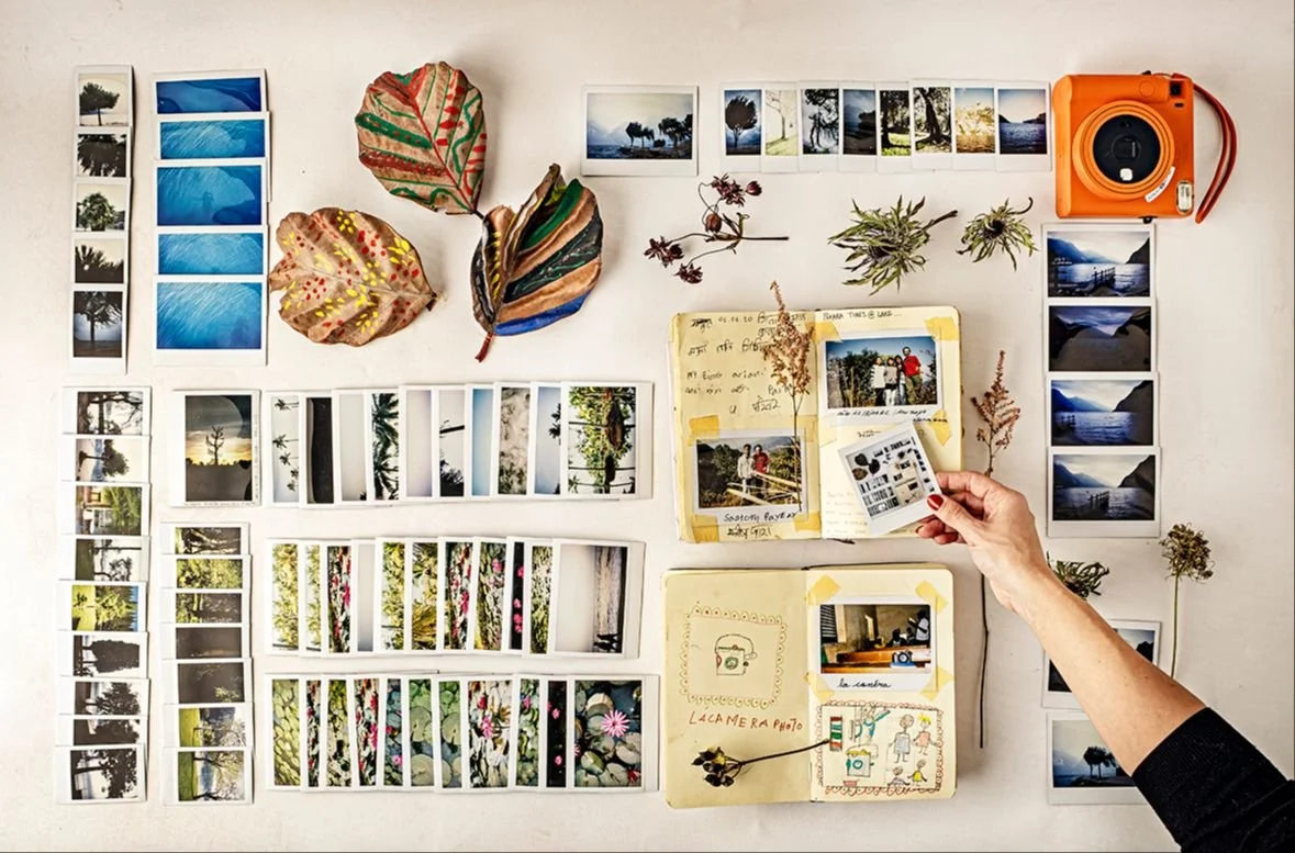 Collection of printed photographs, leaves, and notebooks arranged on a white table for scrapbooking or photo organizing.