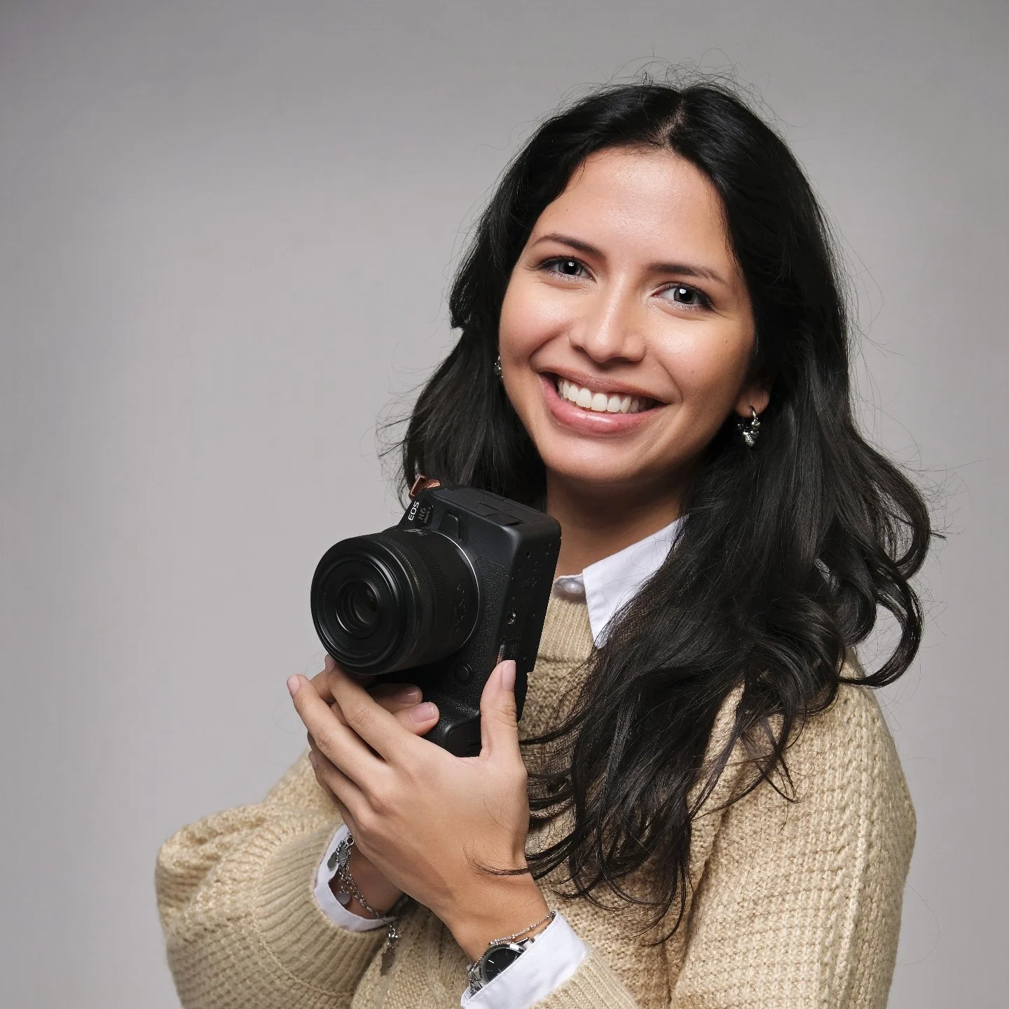 A smiling woman with long dark hair holding a camera in her hands.
