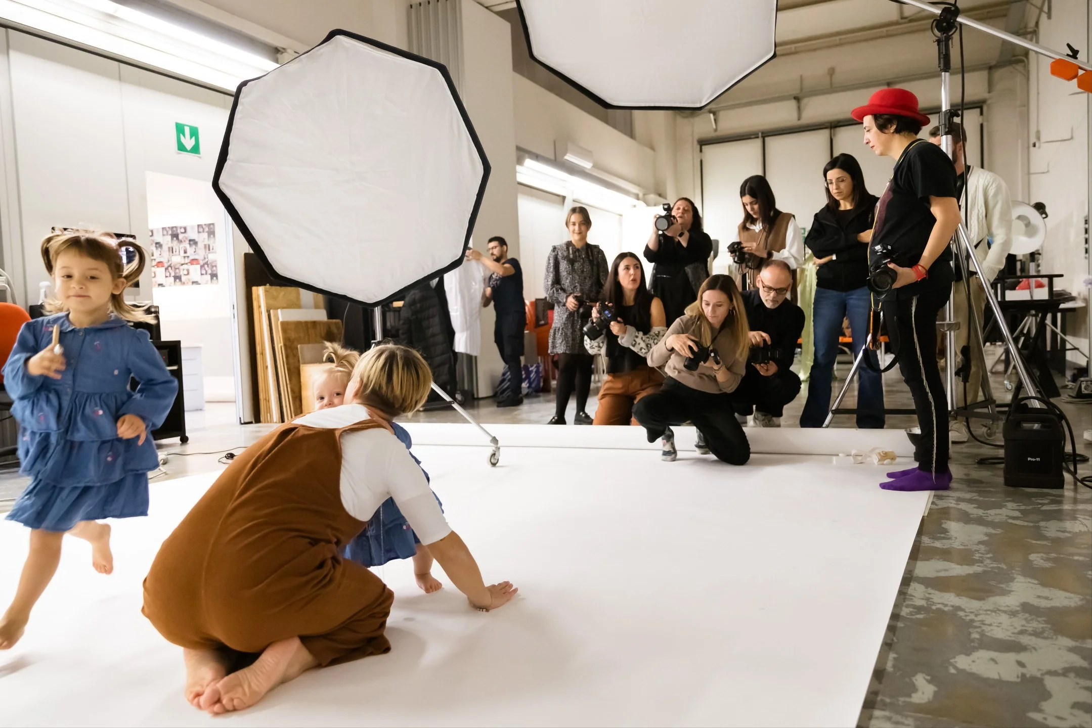 Children posing for a photoshoot on a white backdrop with multiple photographers and crew members capturing the scene in a studio.