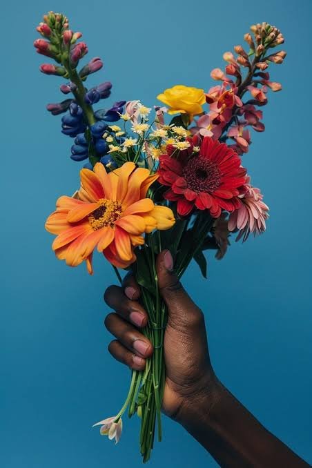A hand holding a colorful bouquet of various flowers against a blue background.