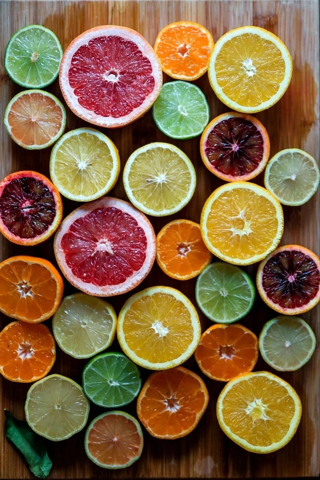 A wooden cutting board with various sliced citrus fruits, including limes, lemons, oranges, grapefruits, and blood oranges.