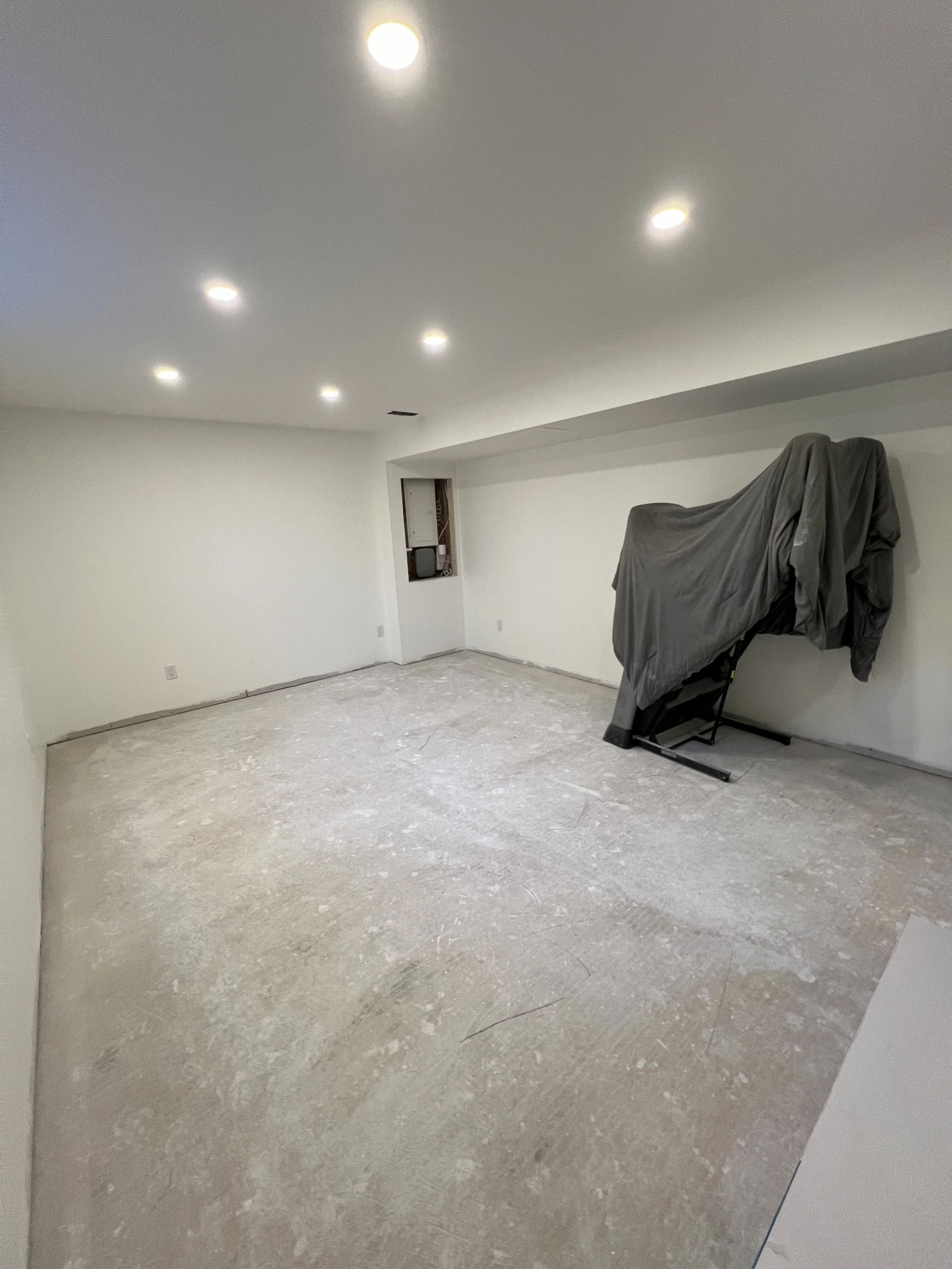 Basement renovation with white walls and ceiling, recessed lighting, and a covered exercise bike in the corner.