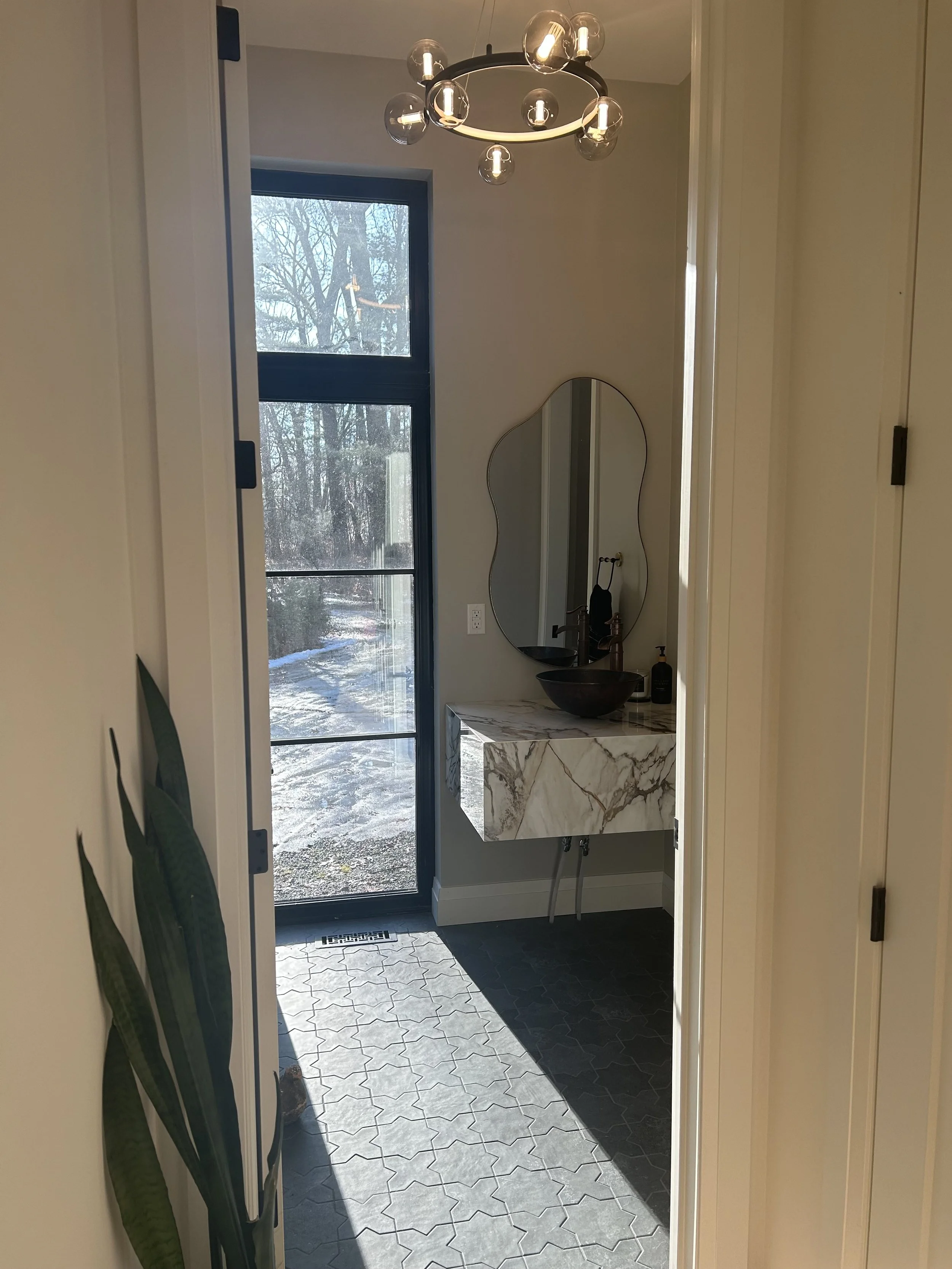 Bathroom with a modern oval mirror, a marble sink, black sink bowls, and a large window showing a snowy outdoor scene.