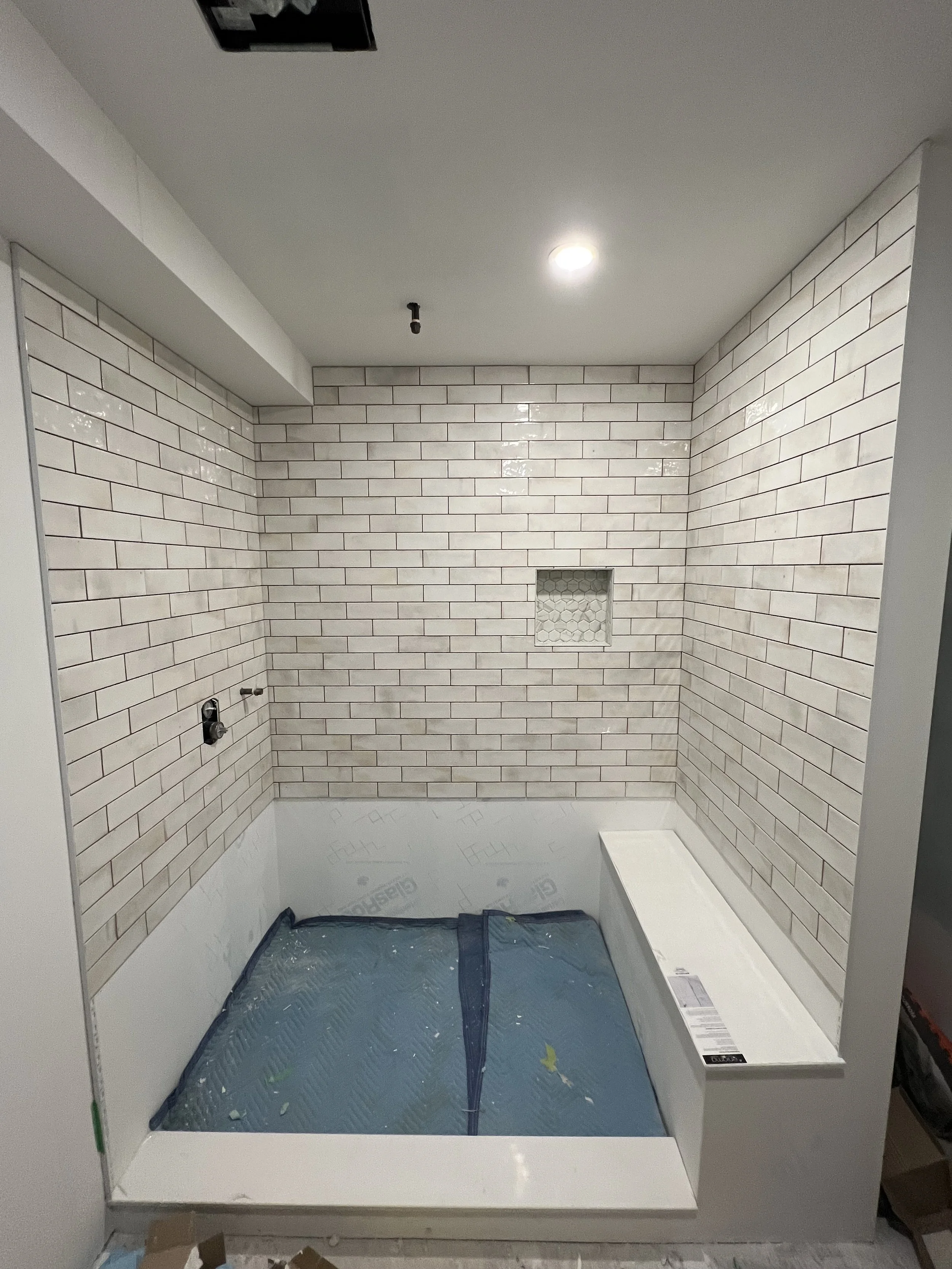 Bathroom renovation with white subway tile walls, a built-in bench, and a recessed niche in the wall for shower storage.