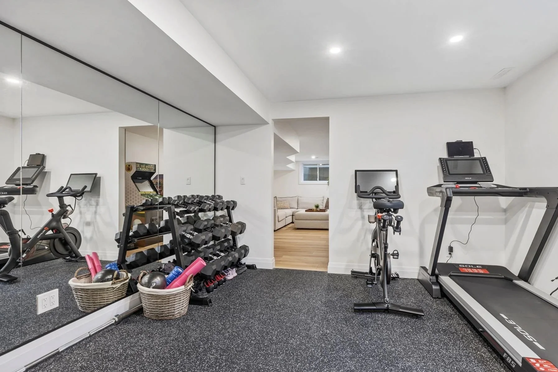 Home gym with exercise equipment including treadmill, stationary bike, dumbbells, and a mirror on the wall.