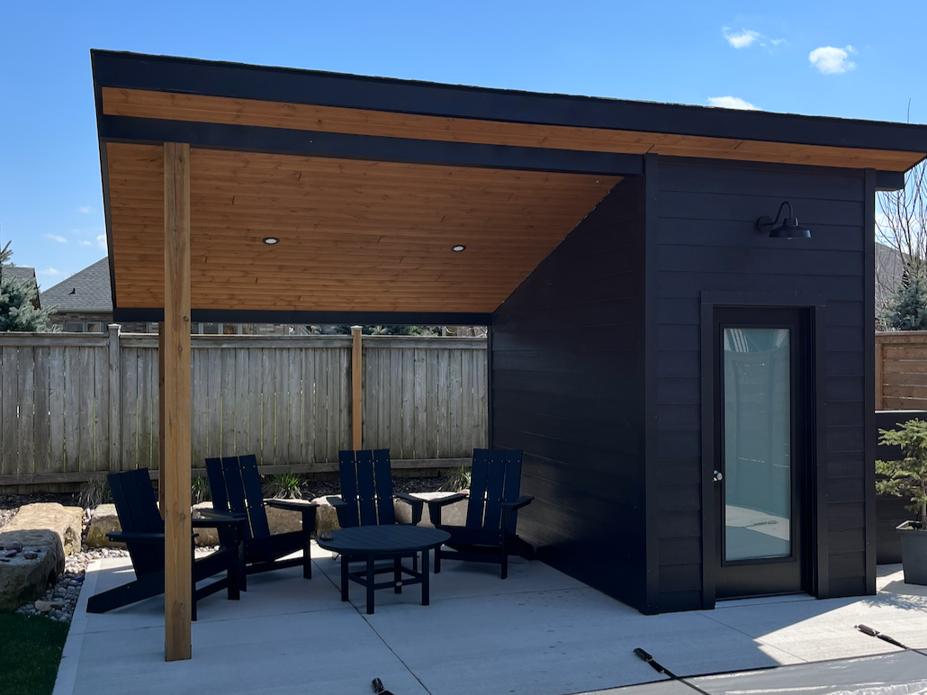 Backyard with a modern black shed, wooden ceiling porch, patio furniture, and a privacy fence under a blue sky