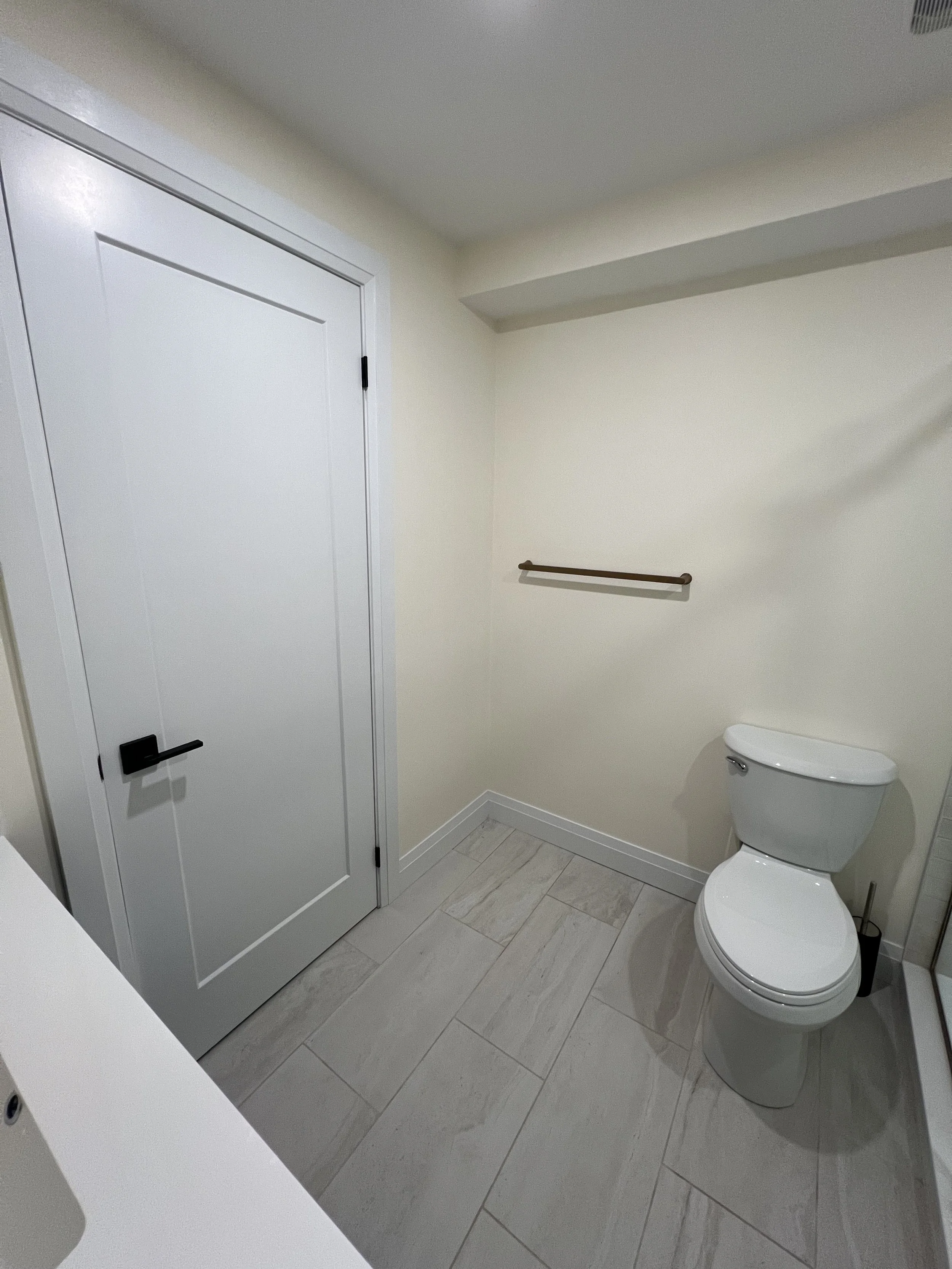 Empty bathroom with a white toilet, beige walls, a towel bar on the wall, and a closed door.