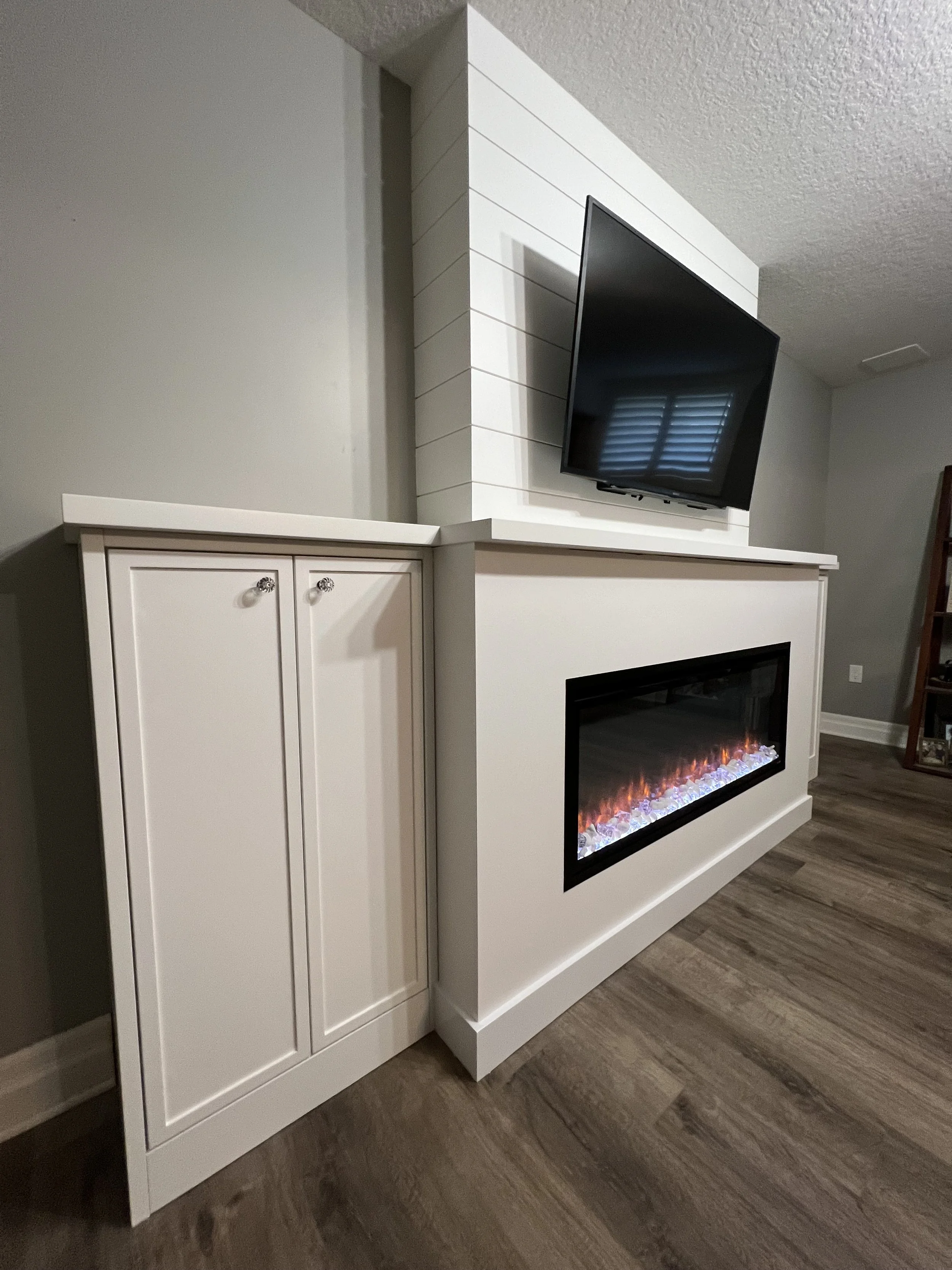 A modern basement renovation with a white fireplace and a mounted flat-screen TV on a white partition wall above the fireplace.