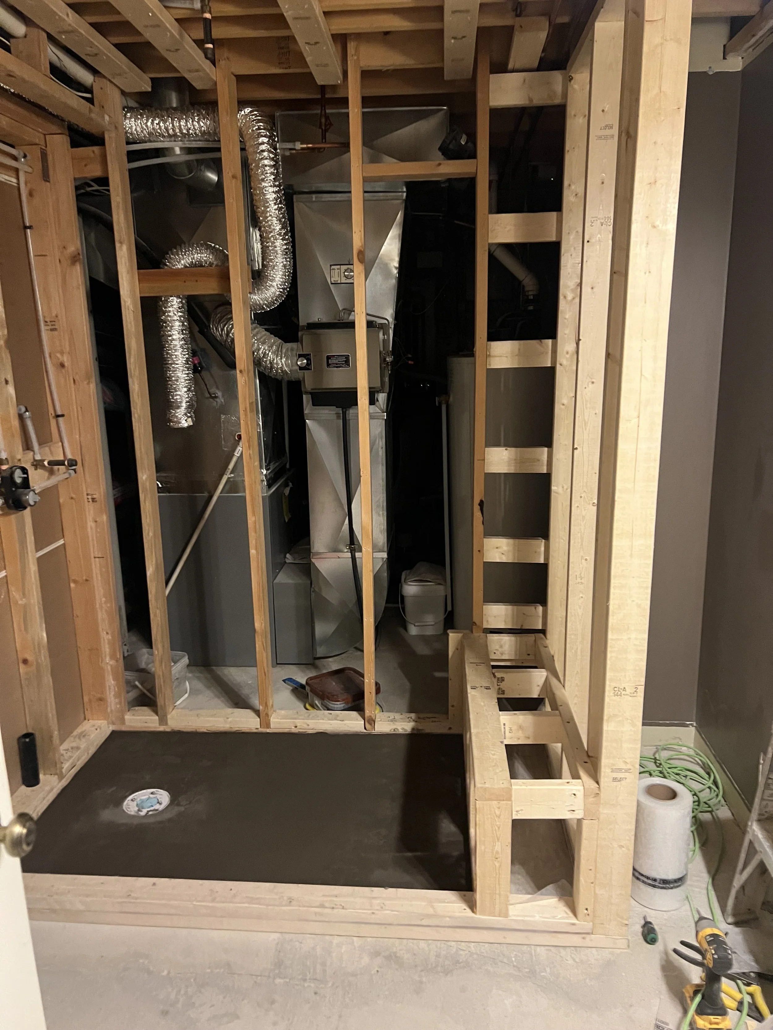 View of a partially constructed room with visible wooden framing, HVAC ductwork, and a concrete floor with a drain.