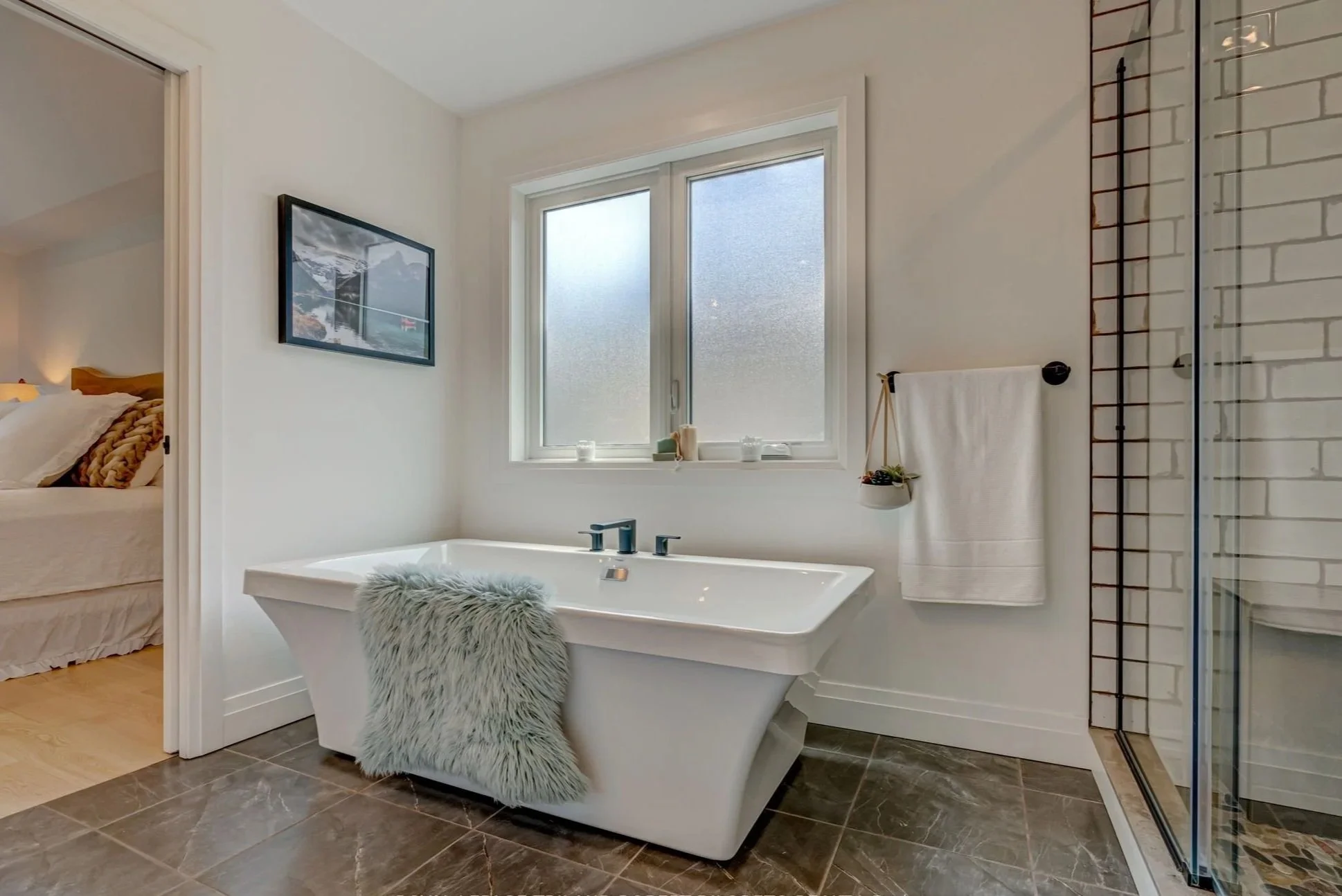 Modern bathroom renovation with a freestanding bathtub, a window, shower enclosure, and bedroom door visible in background.