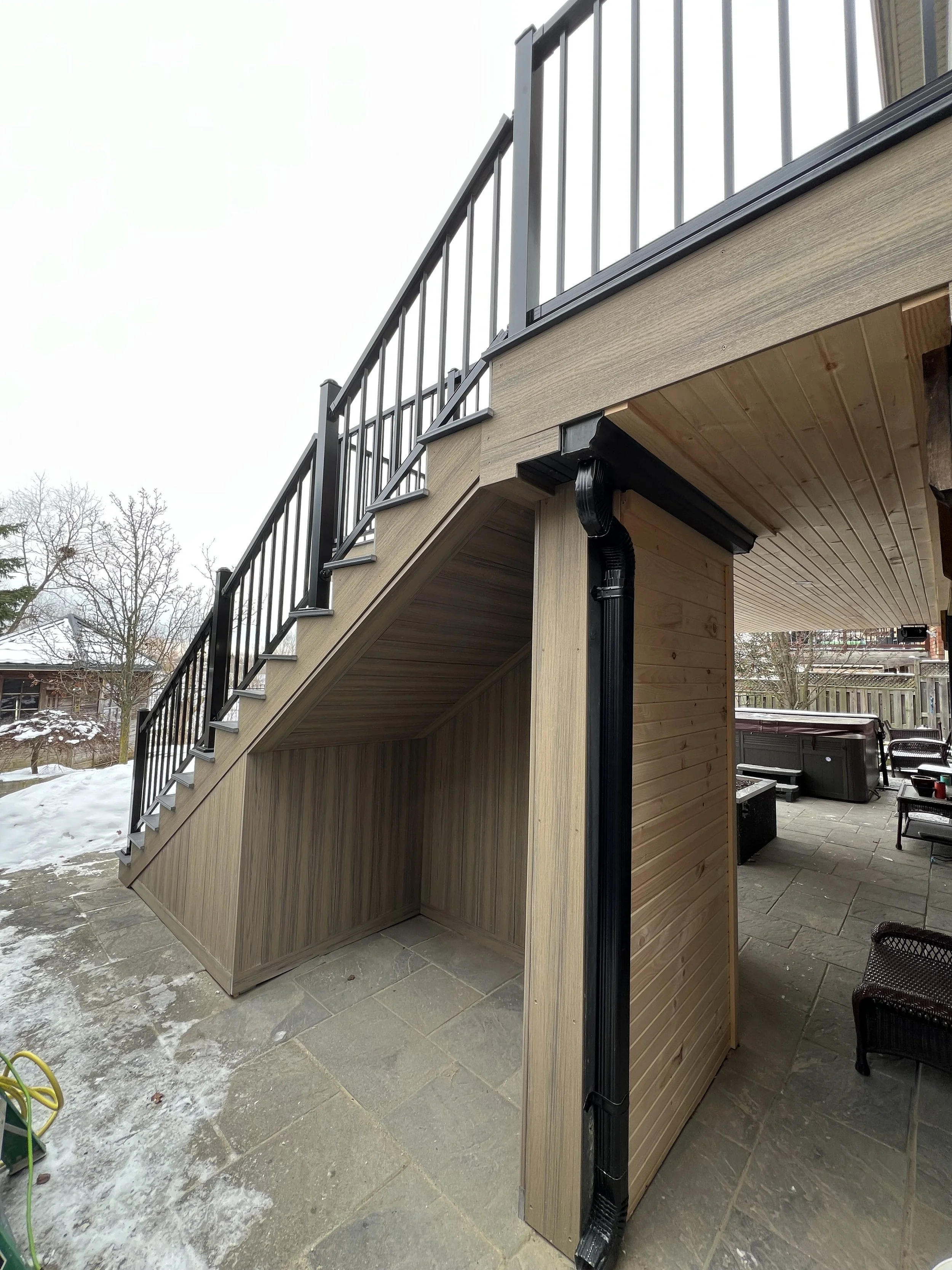 composite deck staircase and patio area with seating, hot tub, and snow on the ground during winter.