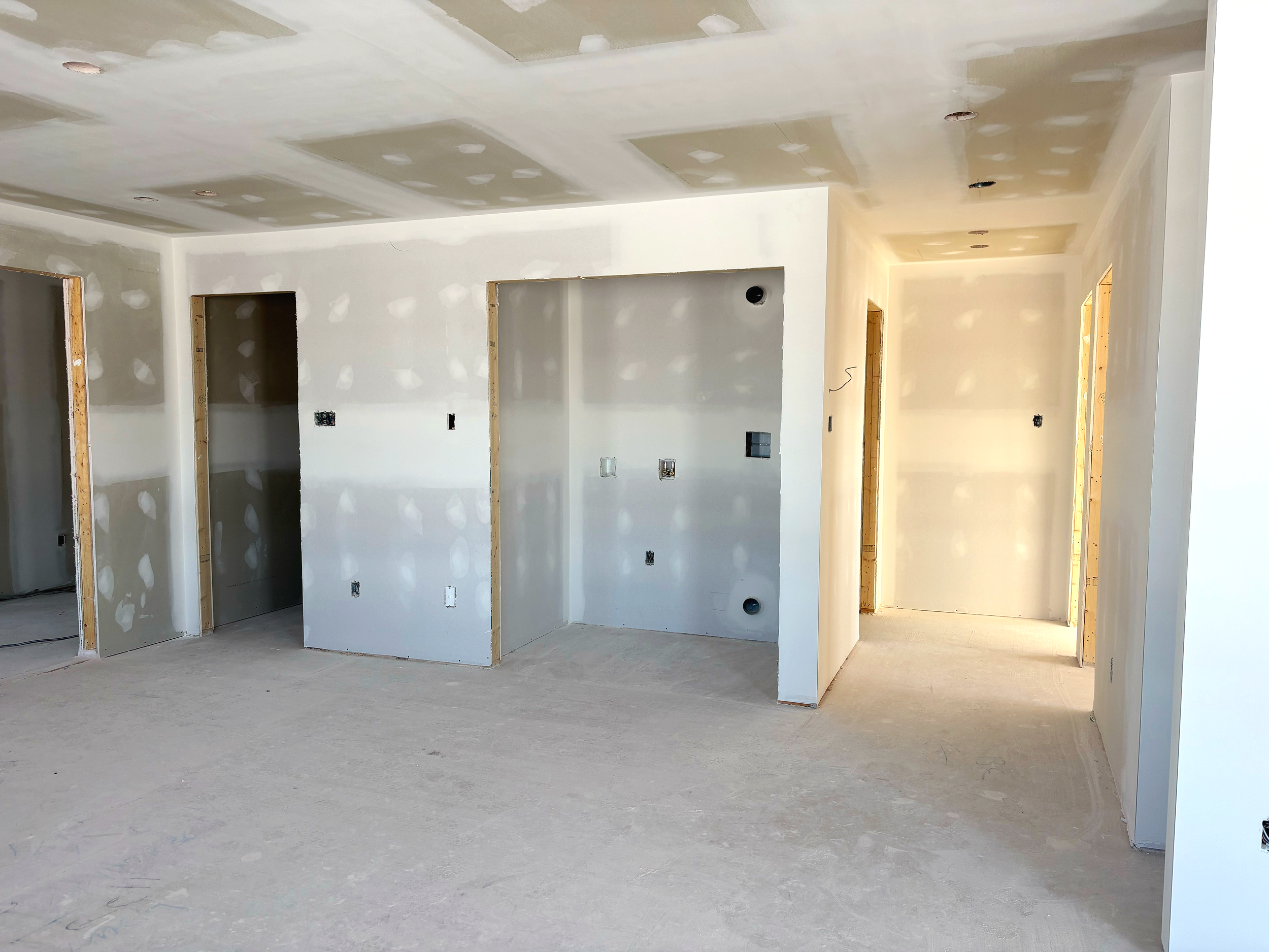 Intérieur en cours de construction avec murs en plaques de plâtre et ouvertures pour portes, sol en béton brut.