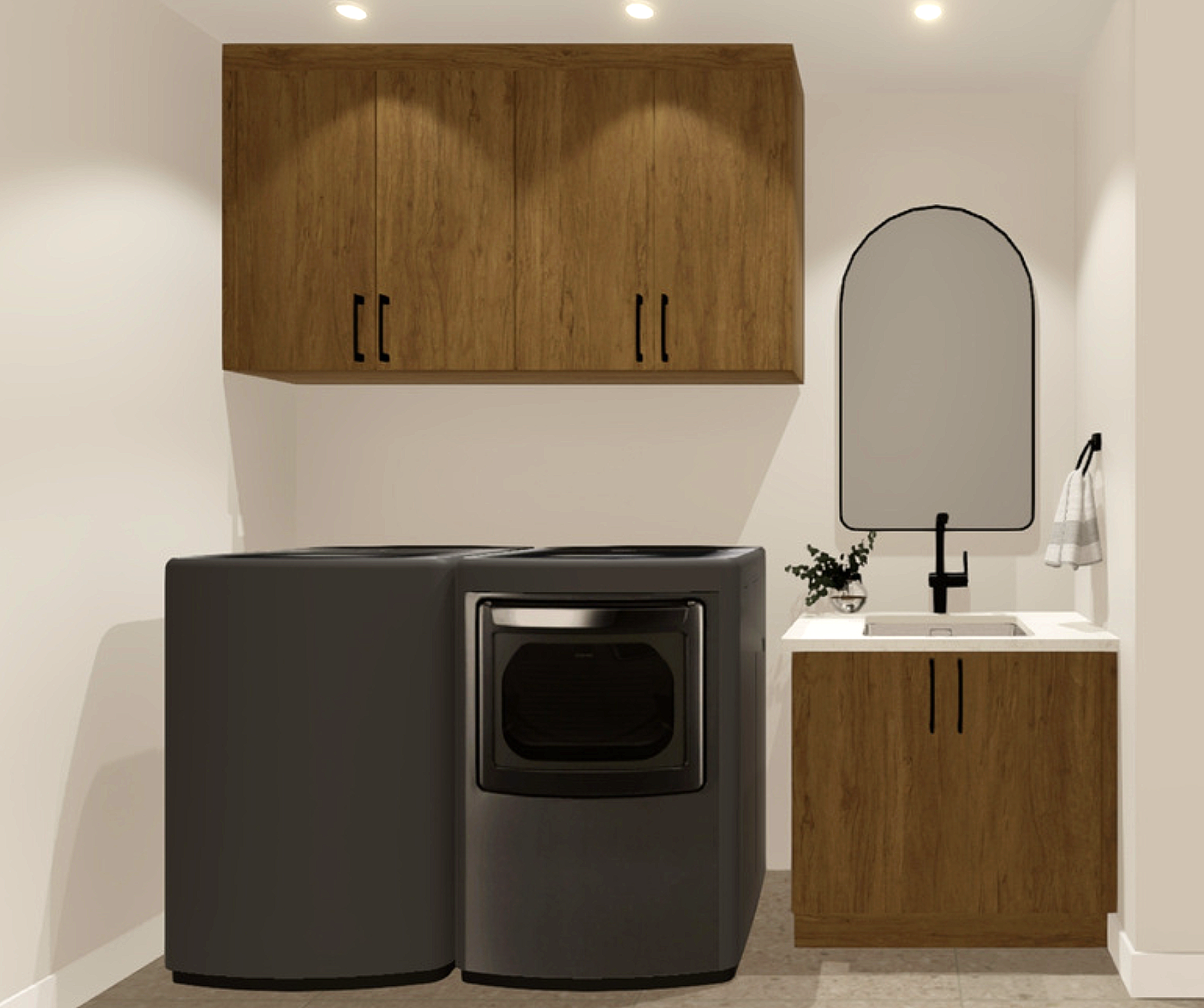 Lave-linge noir avec porte en verre, situé dans une buanderie aux murs blancs, avec un meuble en bois clair au-dessus et un autre sous le évier avec un miroir rectangulaire avec une ardoise noire derrière, une plante verte dans un bol en verre, et une serviette suspendue.