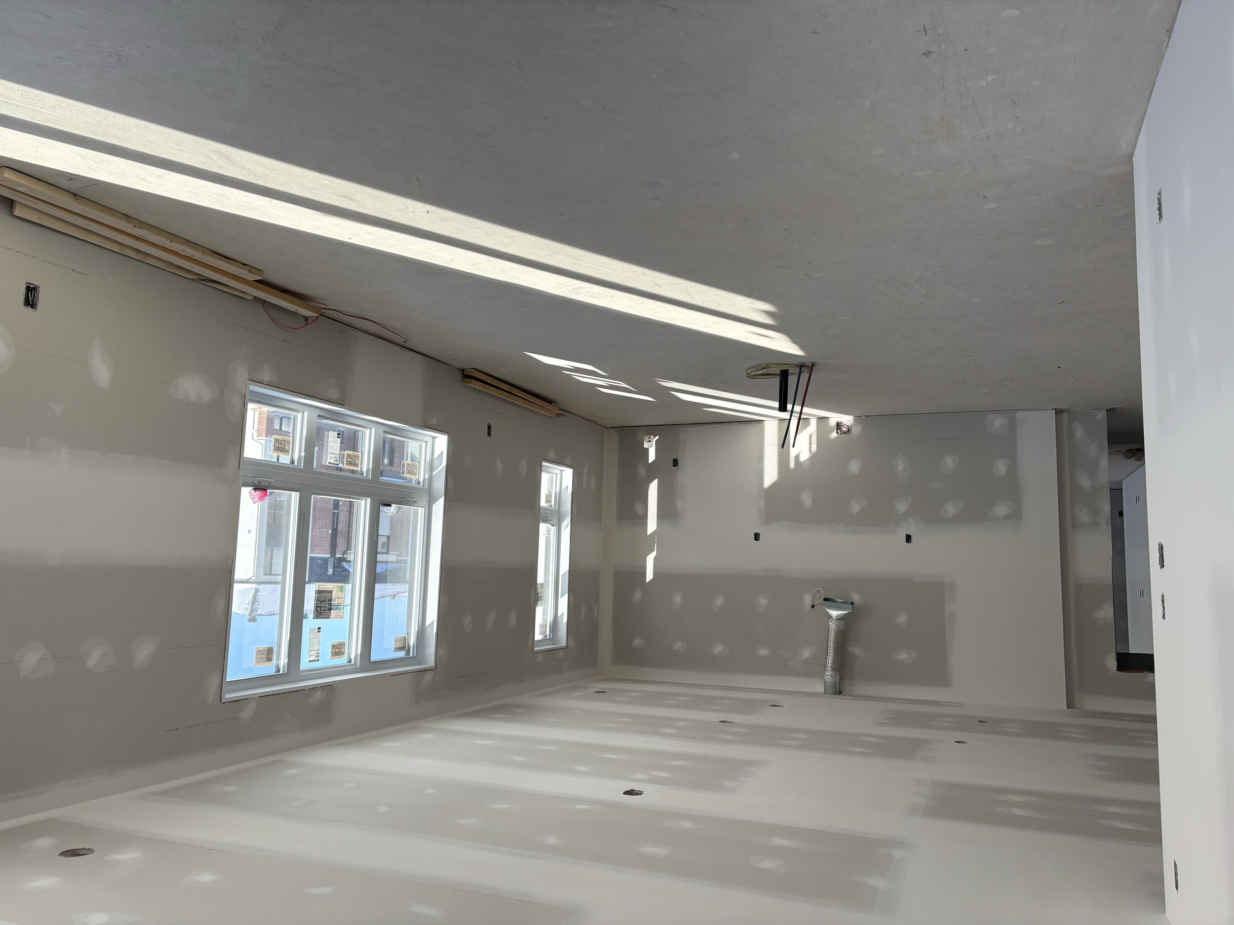 Intérieur en cours de construction avec des murs en plâtre, deux fenêtres, et des installations électriques en place.