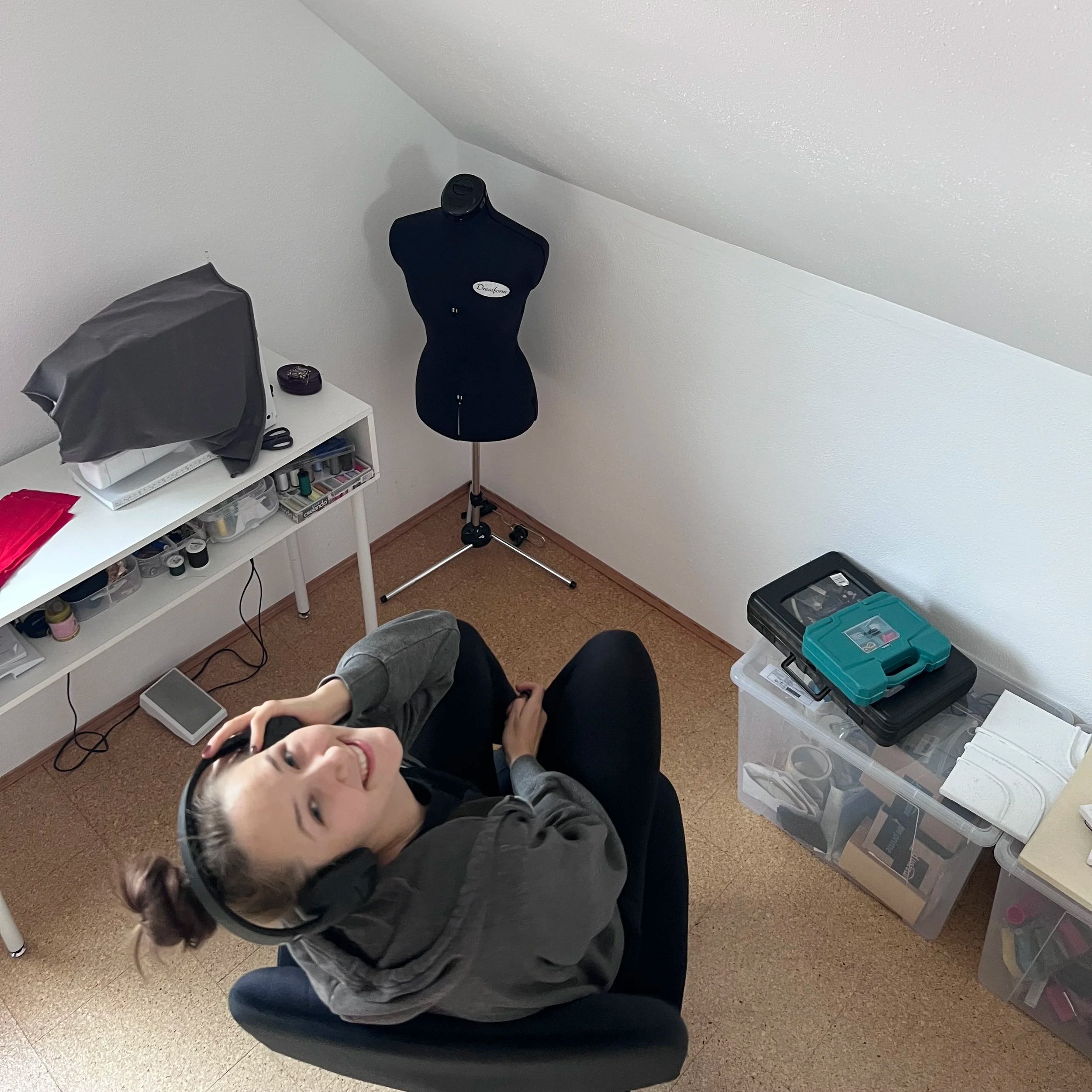 Julian sitzt in einem Raum mit weißen Wänden, trägt Kopfhörer und lächelt in die Kamera, während er auf einem schwarzen Stuhl sitzt.