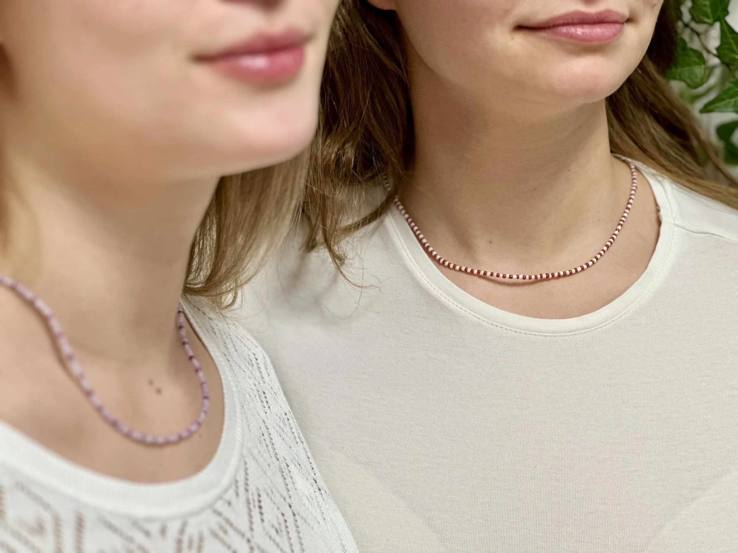 Zwei Frauen tragen Perlenketten und weiße Oberteile, Nahaufnahme der Hals- und Lippenpartie.