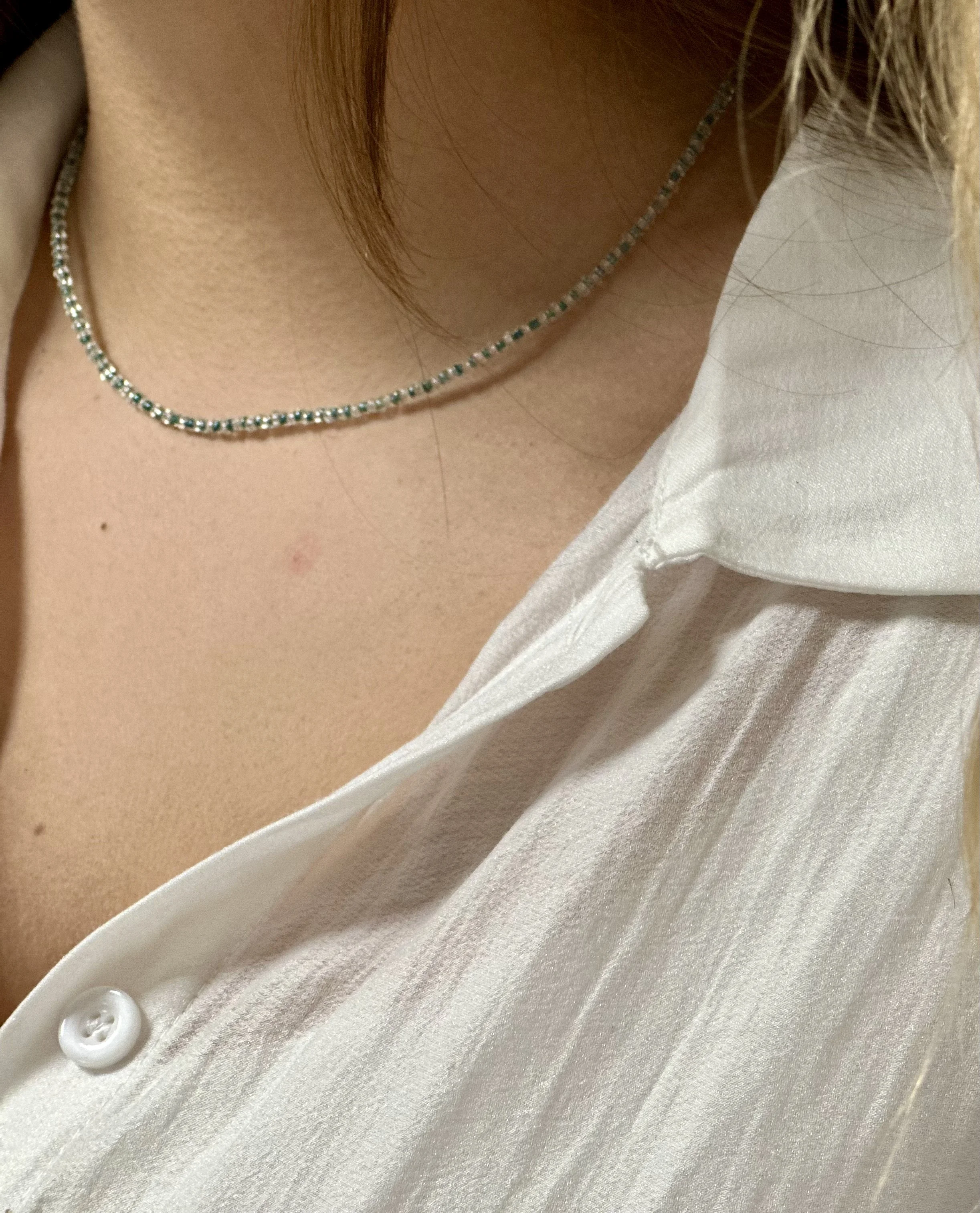 Nahaufnahme eines weißen Hemds mit Perlmuttknopf und einem Silberhalskette, die den Hals schmückt.