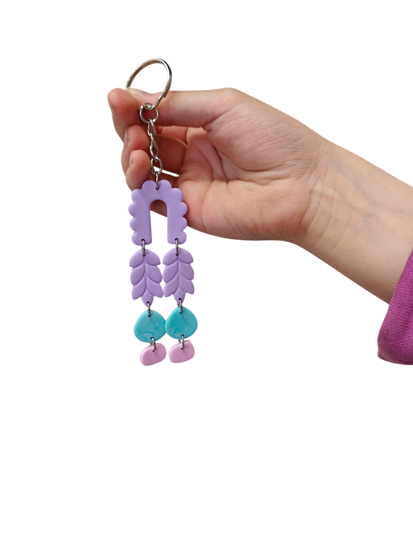 Käsissään pieni käsintehty avaimenperä, jossa on vaaleanpunainen, lila ja turkoosi polymeerisavi. Korupaja lappi sodankylä kaadodesign