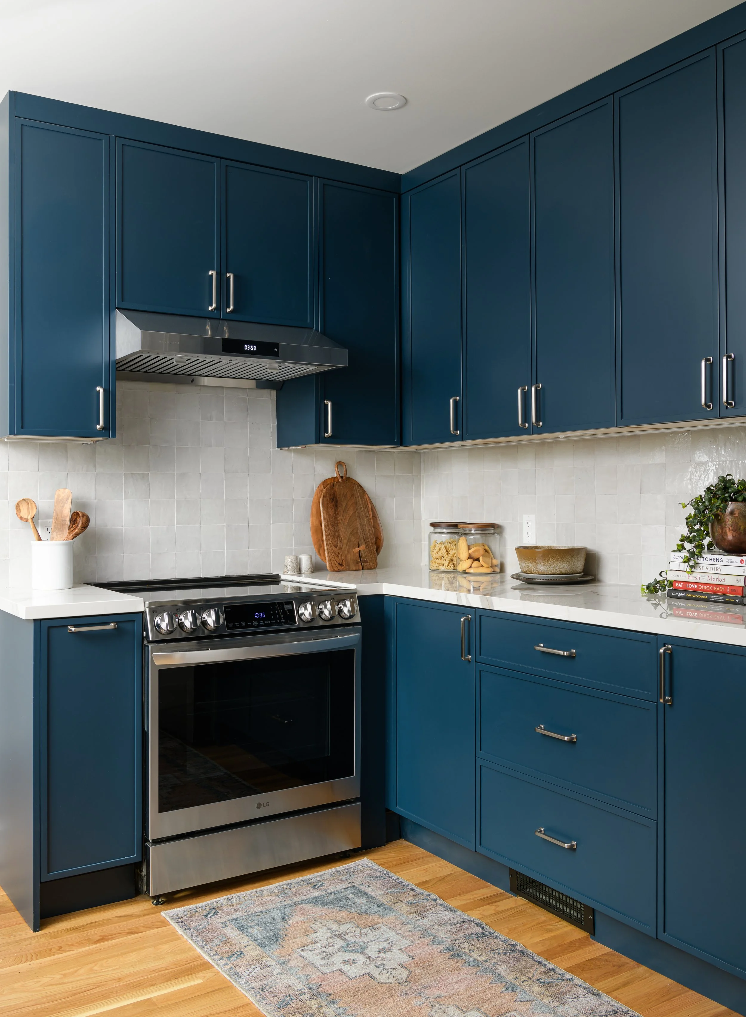 Kitchen with dark blue cabinets, a stainless steel stove, a wooden cutting board, jar of pasta, and a stack of books on the countertop.