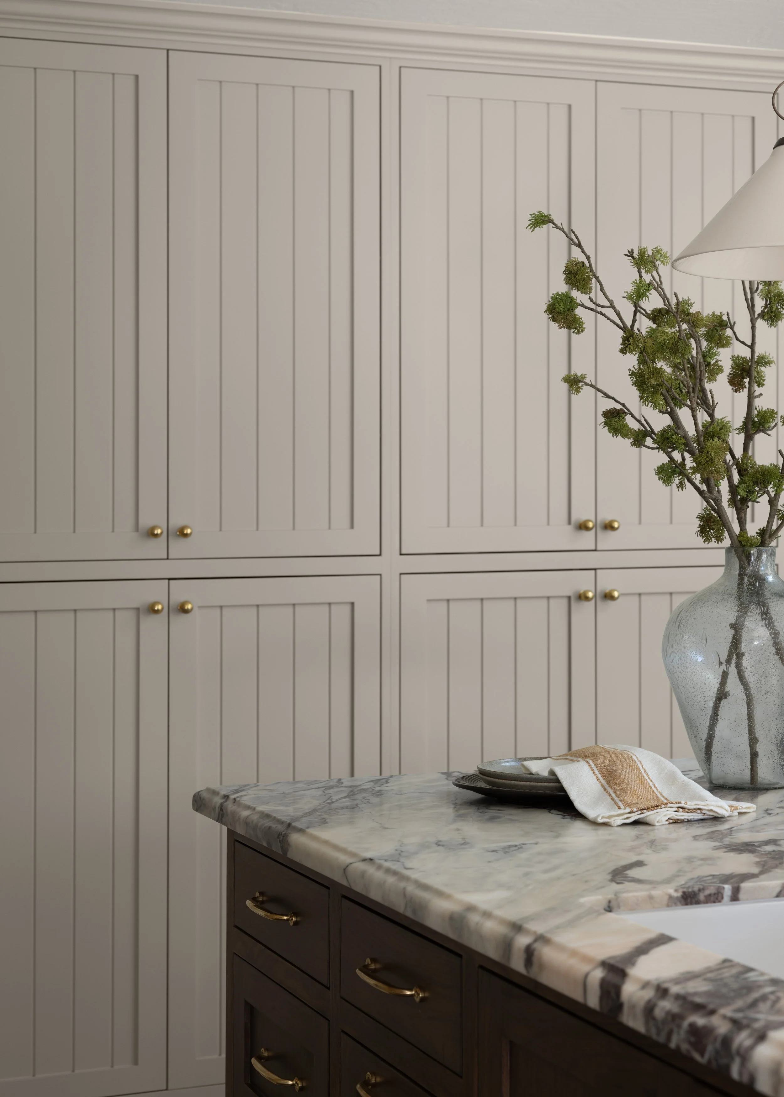 Modern kitchen with white paneled cabinets, a marble countertop, and a vase with branches and greenery on the counter.