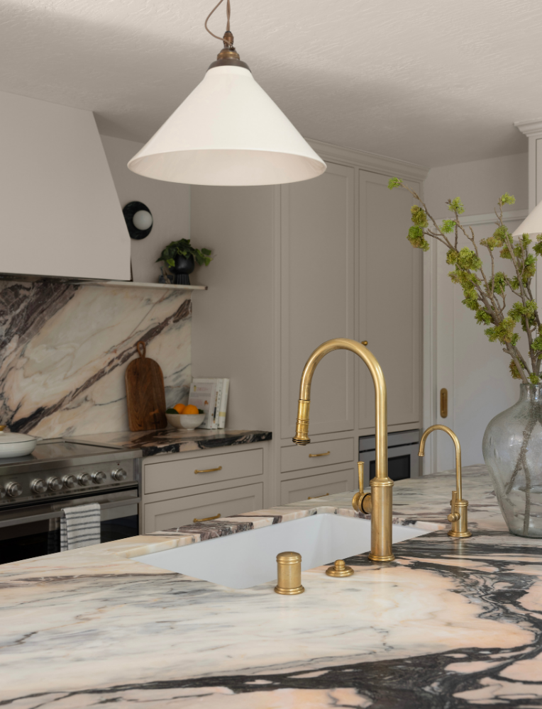 Modern kitchen with marble countertops, gold fixtures, and a white hanging pendant light.