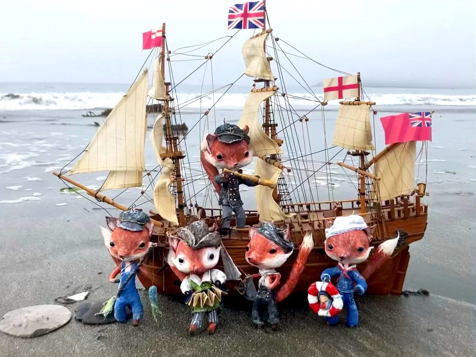 An elaborate miniature pirate ship with Union Jack and English flags on a beach, surrounded by anthropomorphic animal figures dressed as pirates.