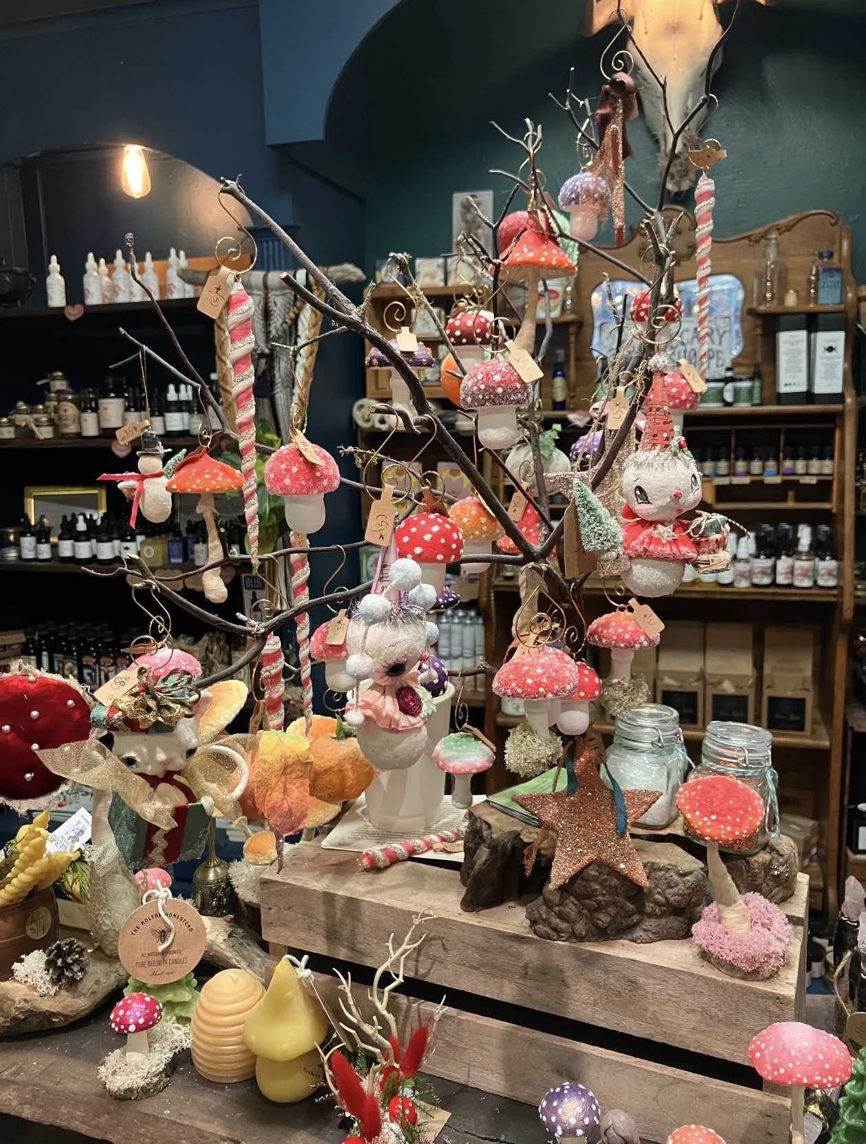 Decorative Christmas ornaments shaped like mushrooms, fairies, stars, and other whimsical figures on a display table in a shop.
