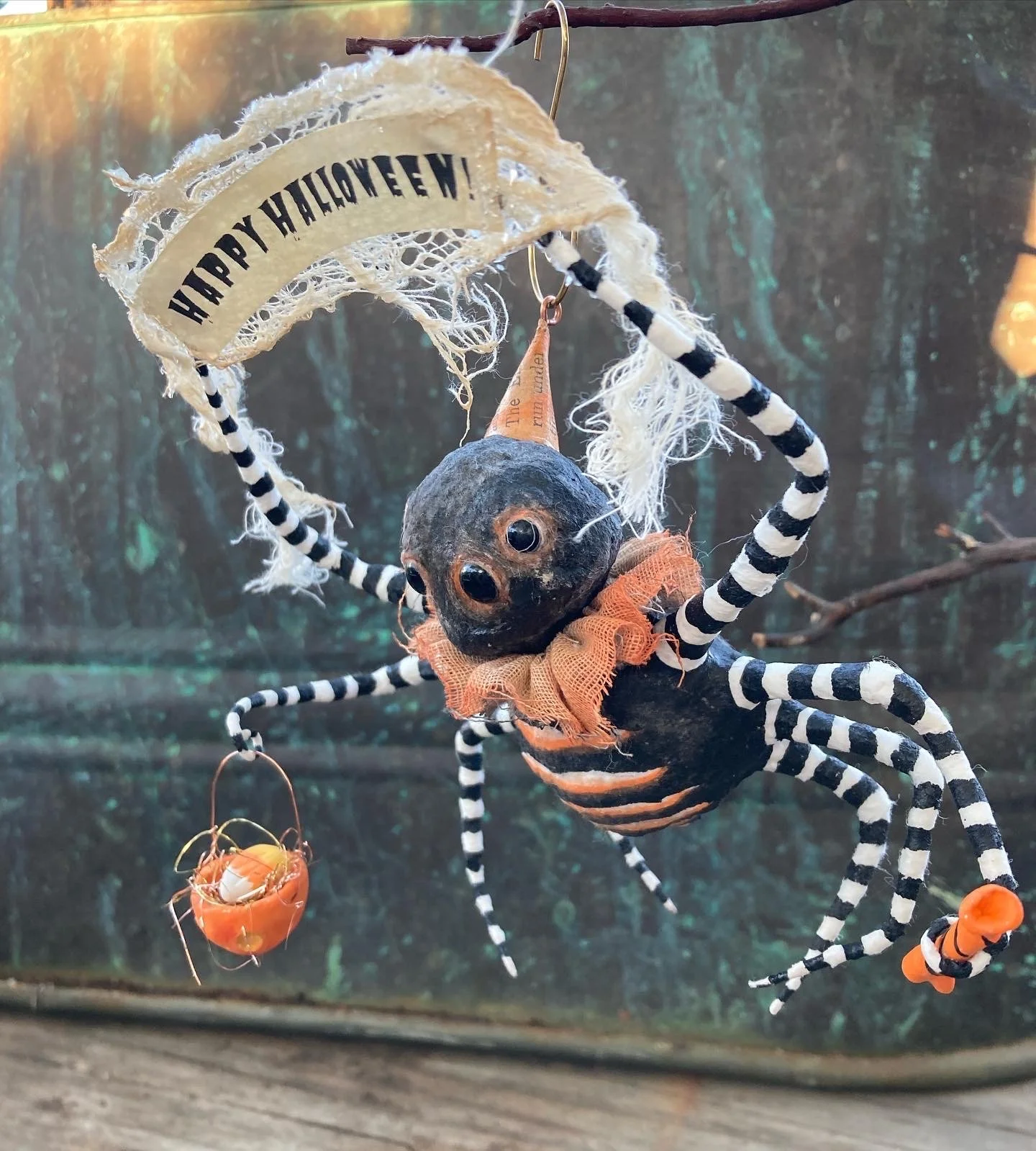 A decorative Halloween spider with black and white striped legs, a black body, and orange accents hanging against a dark outdoor background.