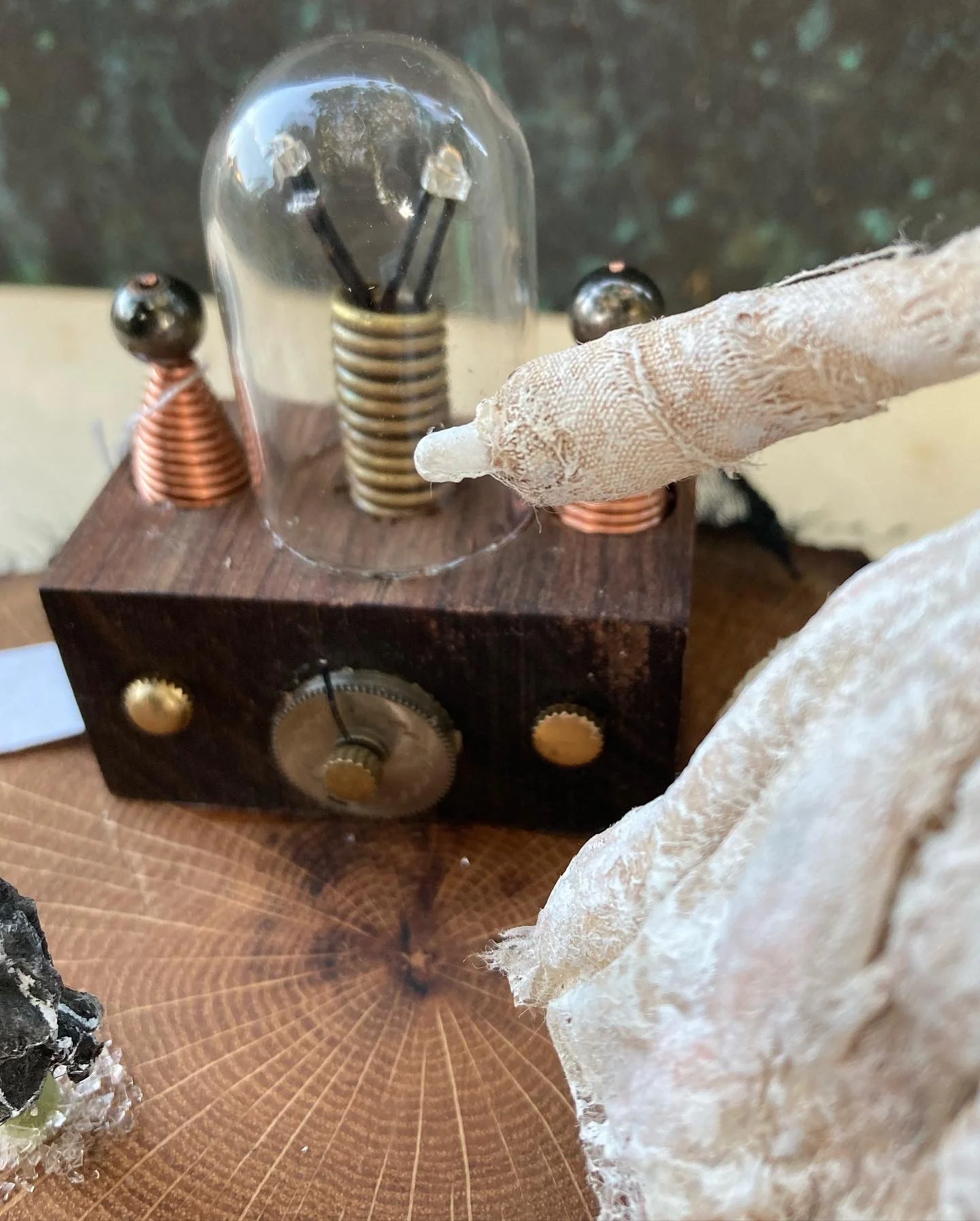 A vintage mechanical device with a wooden base, copper coils, and metal components, surrounded by decorative elements such as dried leaves or fabric.