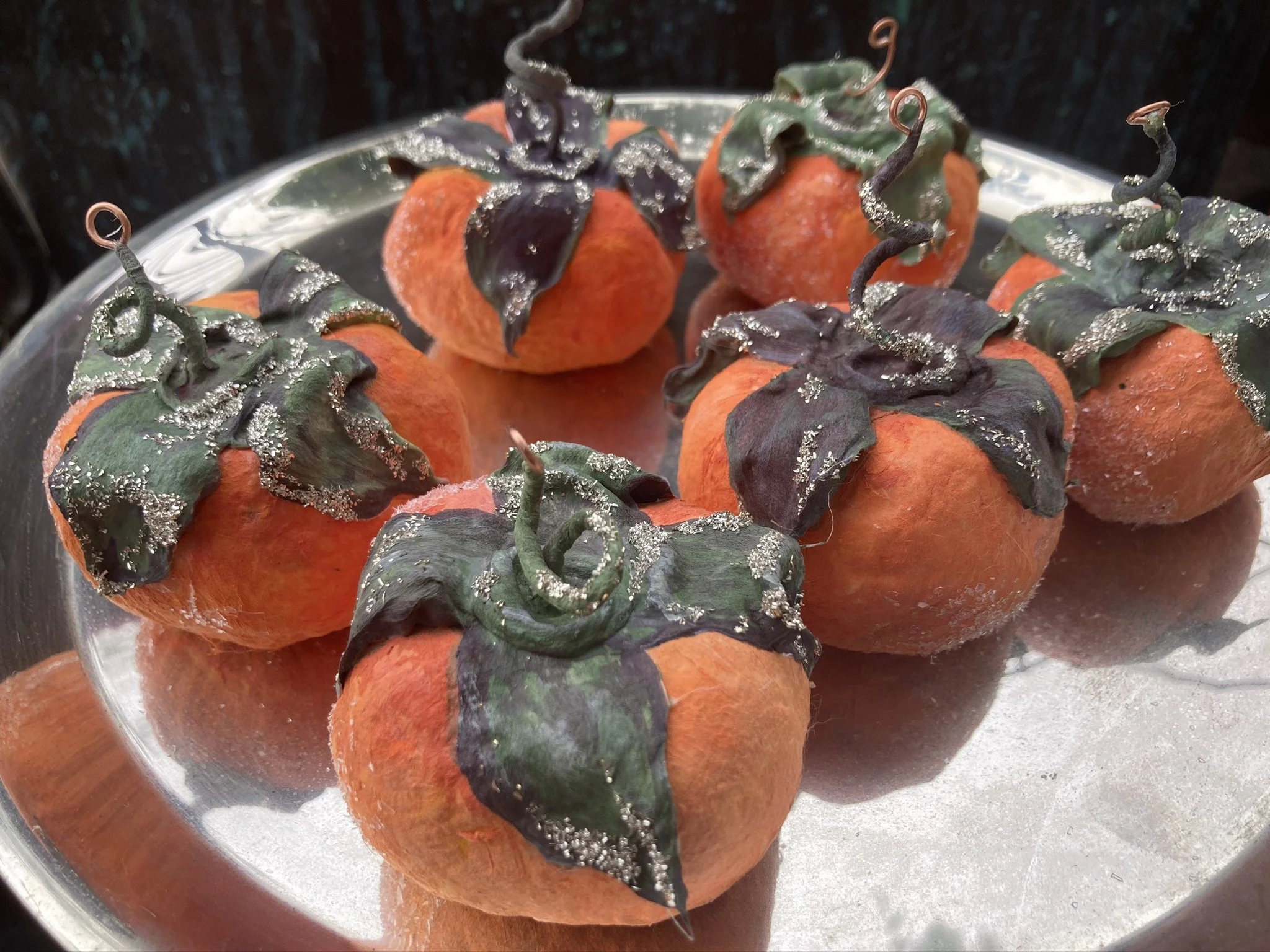 A tray of orange pumpkins decorated with dark purple and green leaves, accented with silver glitter, in a close-up view.