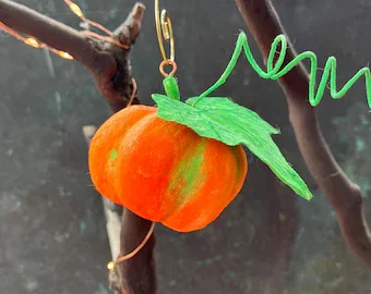 Hanging orange pumpkin-shaped ornament with green leaf and tendril, attached to tree branch.