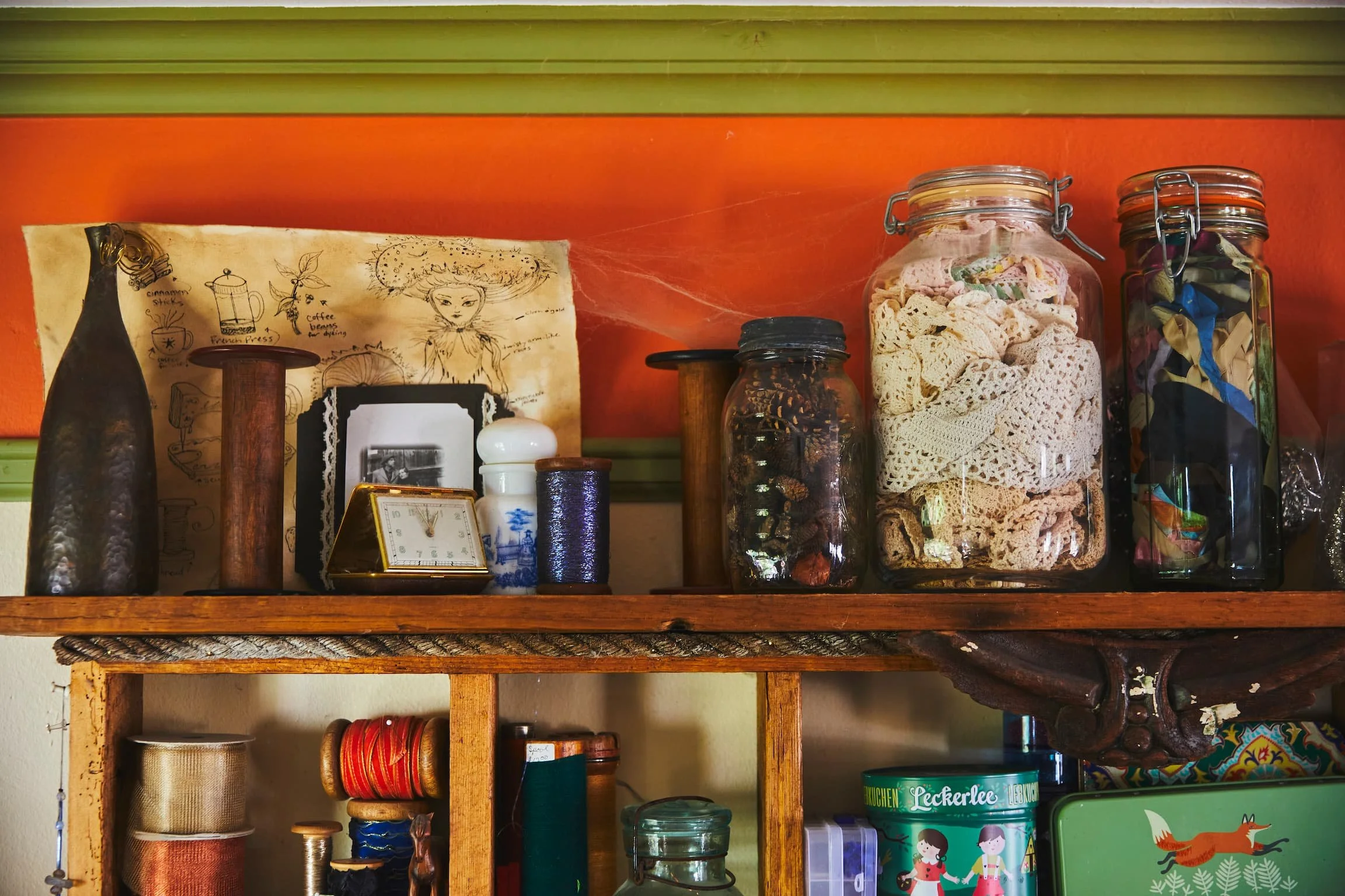 A wooden shelf with jars, boxes, and decorative items in front of a orange and green wall.