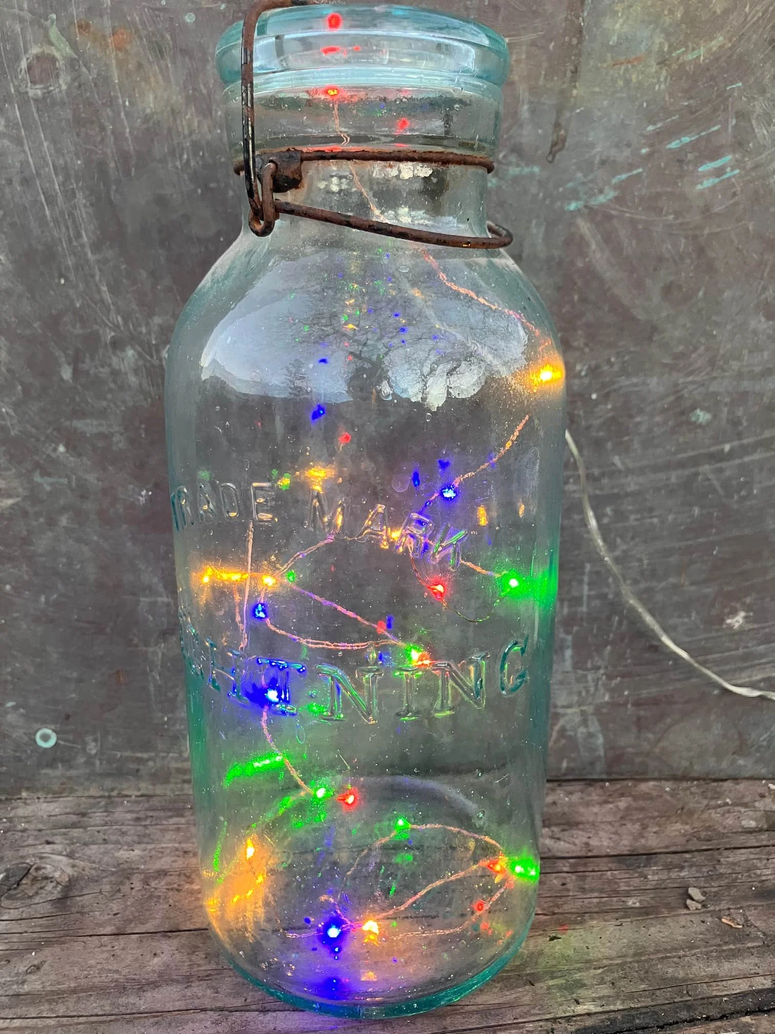 A glass bottle filled with tiny colorful string lights resting on a wooden surface.