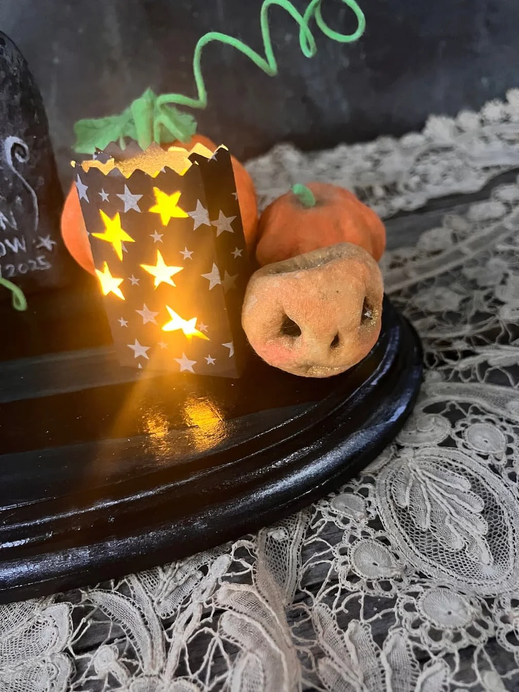 Decorative Halloween sculpture with a lit paper pumpkin lantern, fake pumpkins, and a doughnut shaped like a pig's face with a snout, on a lace tablecloth.