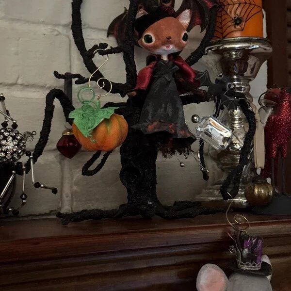 Decorative Halloween figurine of a tree with a squirrel dressed as a witch, with a pumpkin hanging from a branch, surrounded by other Halloween decorations.