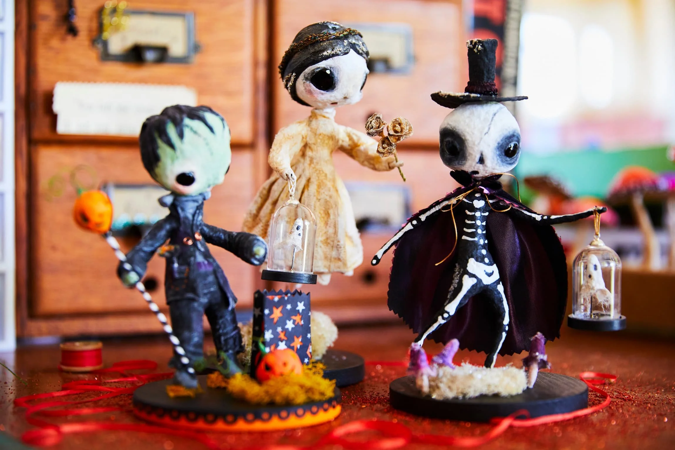 Halloween-themed handcrafted figurines depicting skeletons with large eyes, dressed in costumes and accessories, displayed on a table with festive decorations.