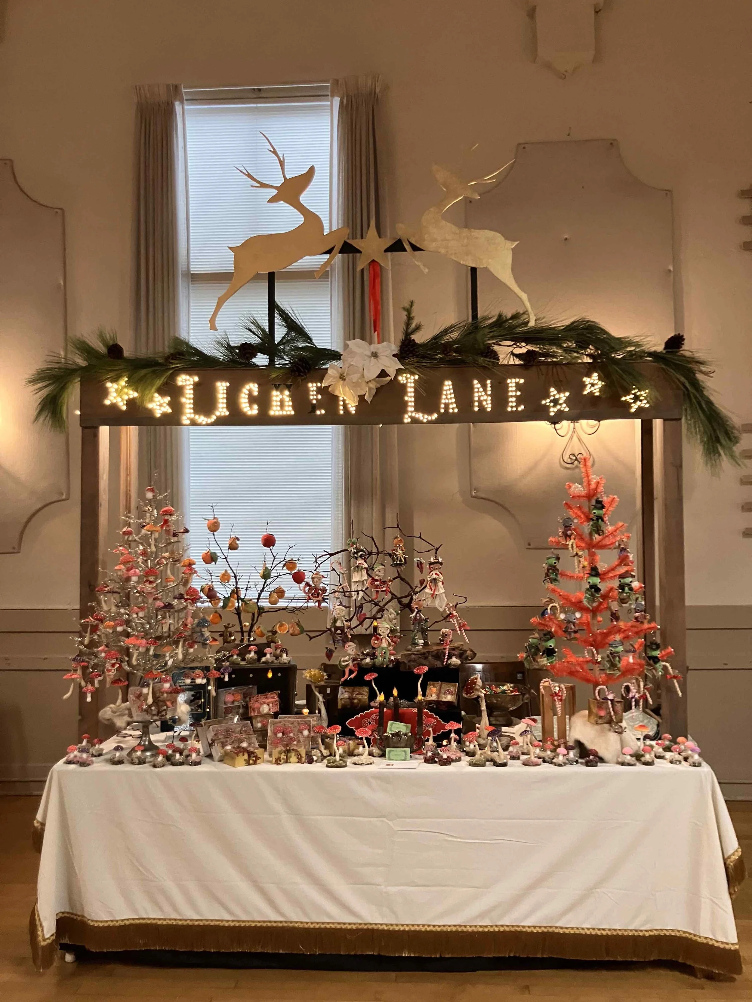 A display of various Christmas ornaments and decorations on a table, with Christmas trees, figurines, and a banner with the words 'LUCKEN LANE' lit with lights, in a festive setting.