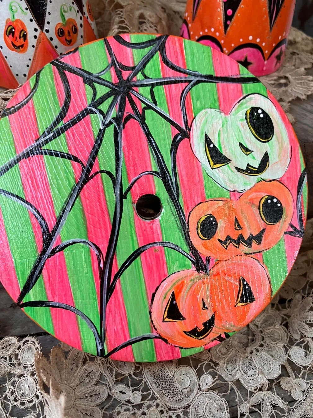 Colorful paper plate hand-painted with Halloween pumpkins and a spiderweb, featuring bright colors like pink, green, orange, and black.