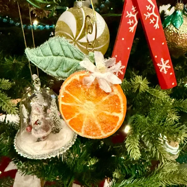 Christmas tree decorated with ornaments, including a dried orange slice, a silver ornament, and a red ribbon