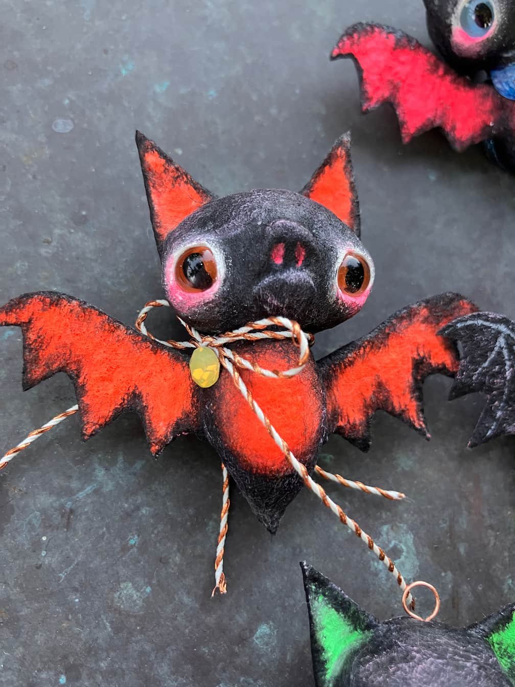 A Halloween decoration resembling a bat with a pig's face, large eyes, and red and black wings, tied with a decorative string.