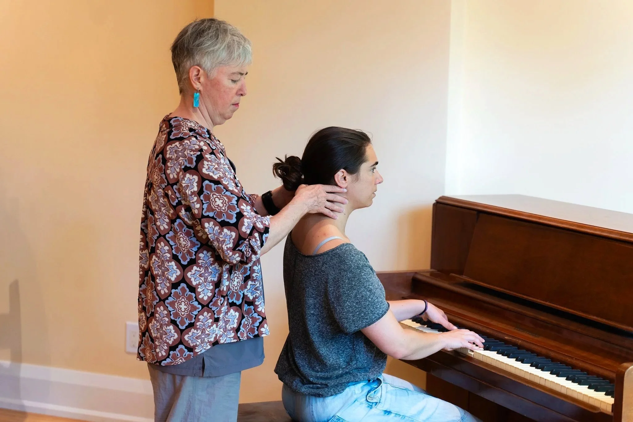 An older woman is receiving a neck adjustment from a younger woman who is playing the piano.