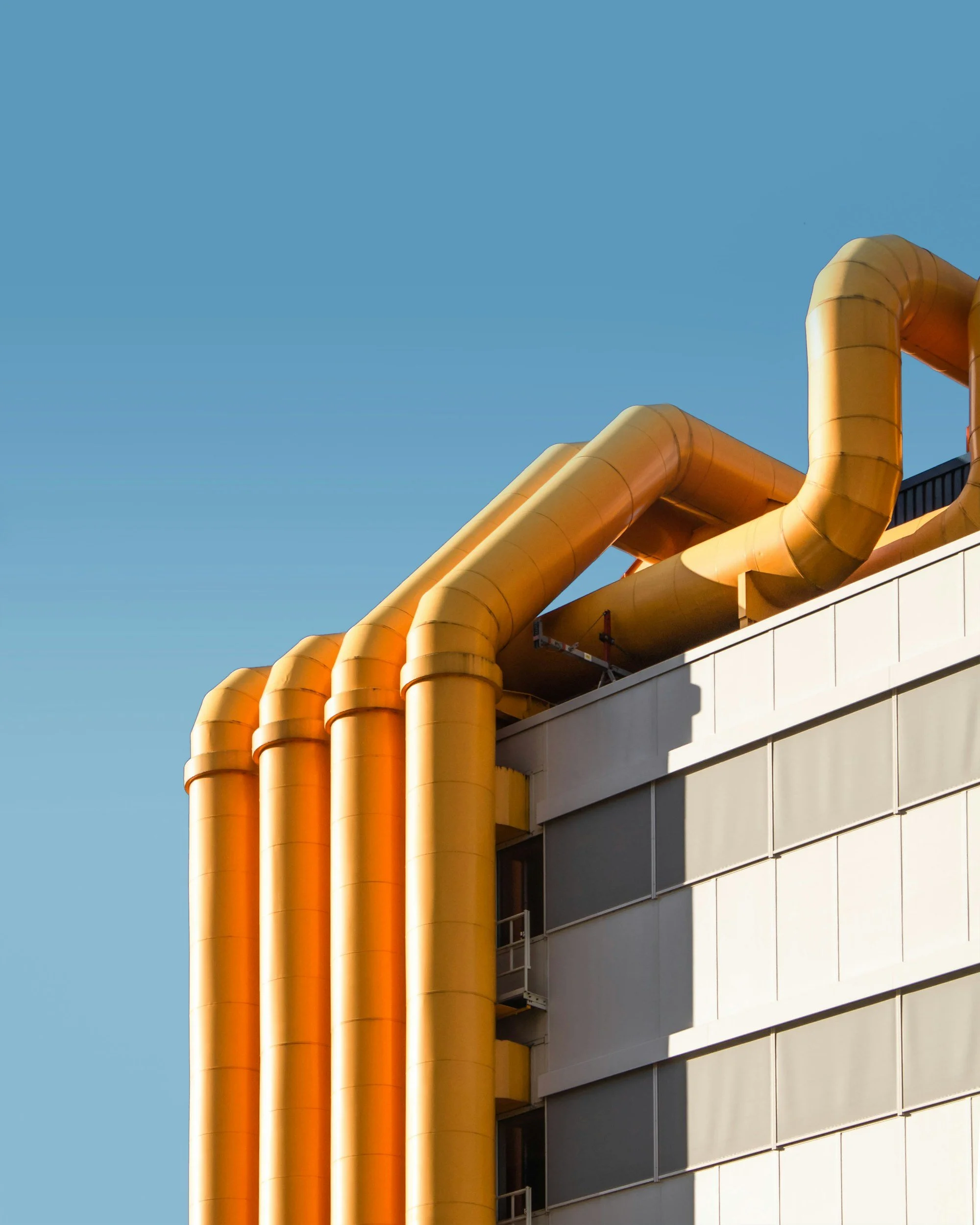 Yellow industrial pipes on the exterior of a building against a clear blue sky.