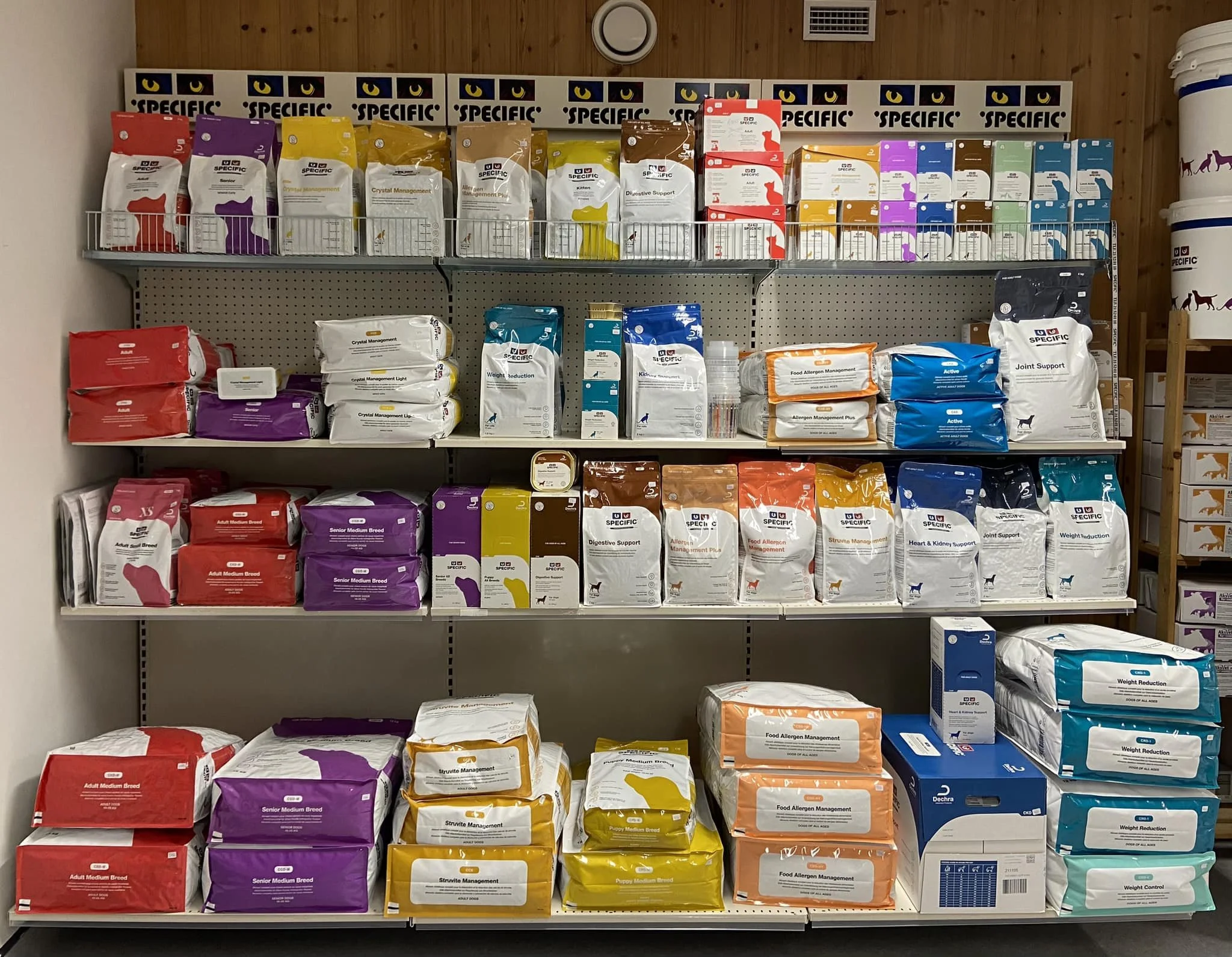 Reol med ulike typer dyrefôr og kosttilskudd i poser og bokser, sortert etter type og størrelse.