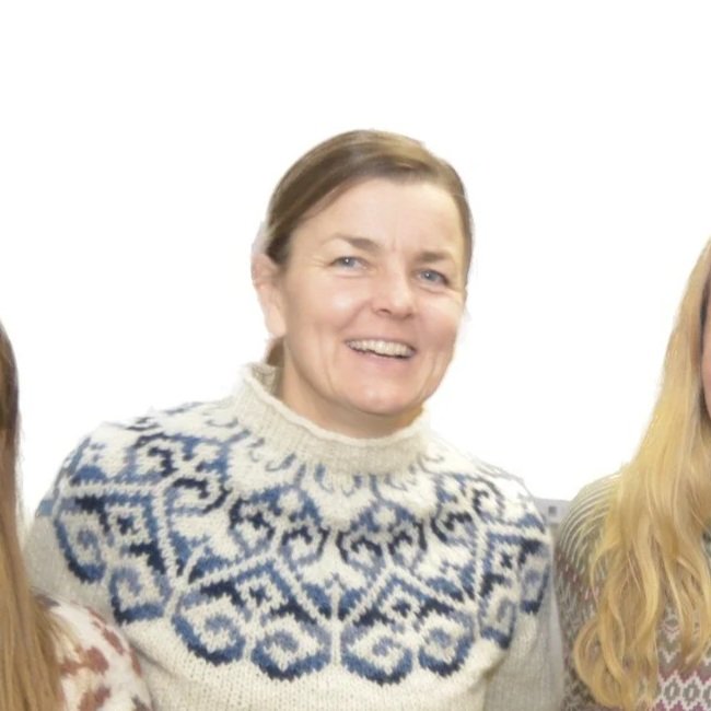 En kvinne med kort brunt hår iført en hvit genser med blå mønster.