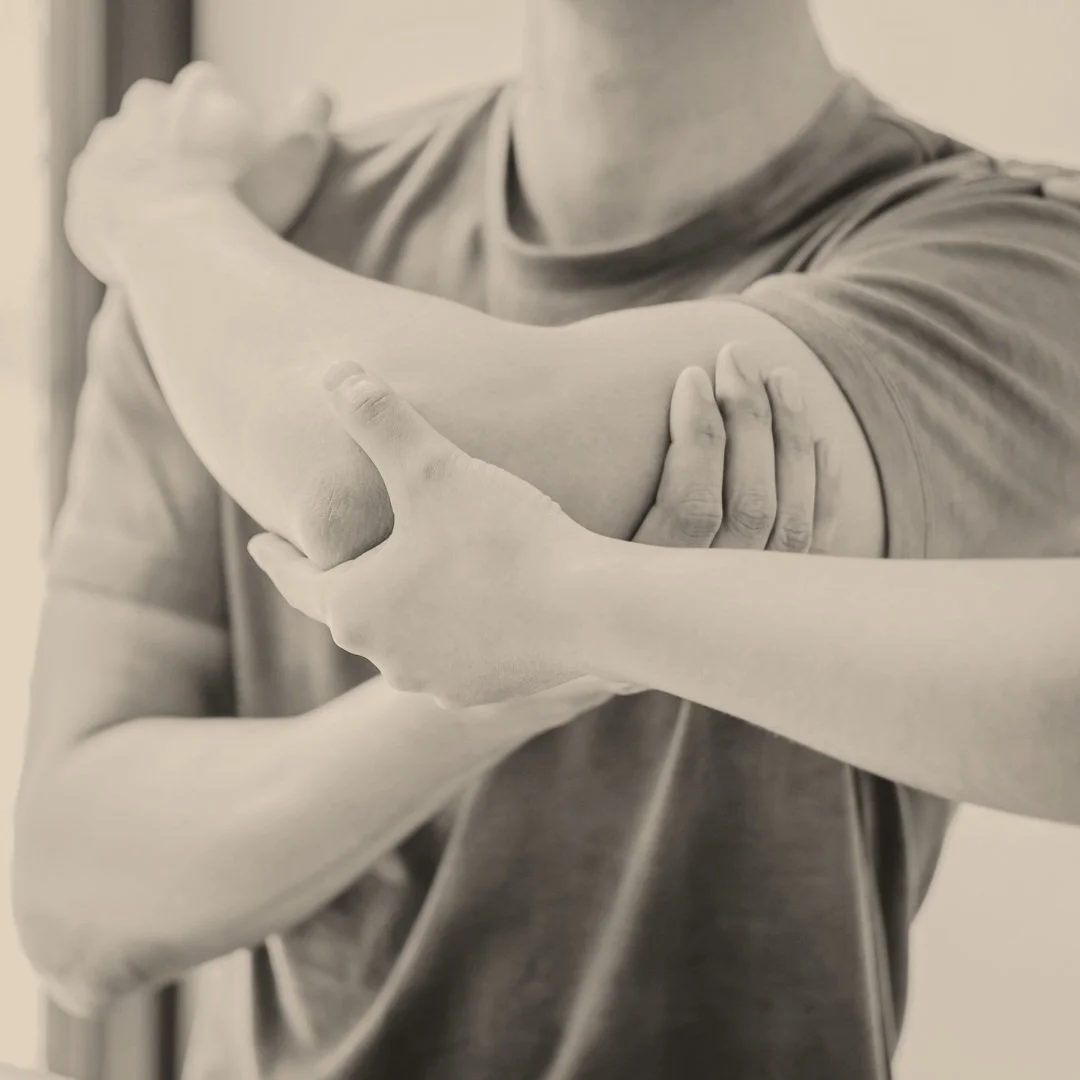 Person performing arm stretch behind head, hands grasping elbow for stretch, wearing a t-shirt.