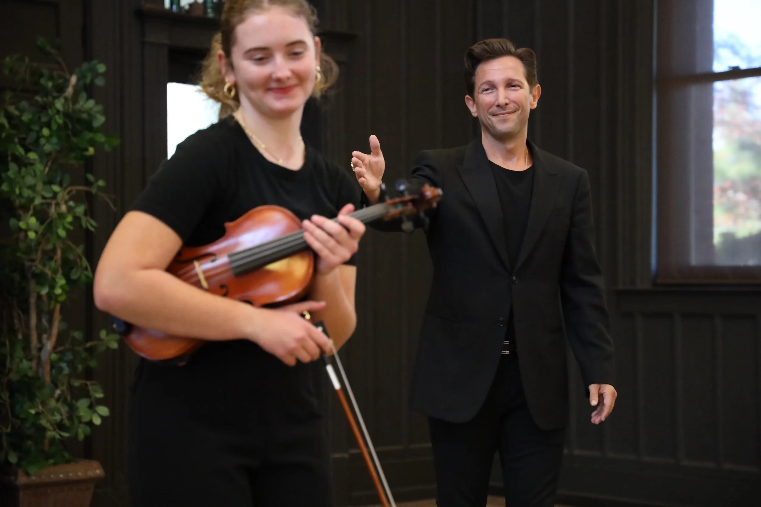 Aaron Blake in a black suit, applauding a young woman with a violin.